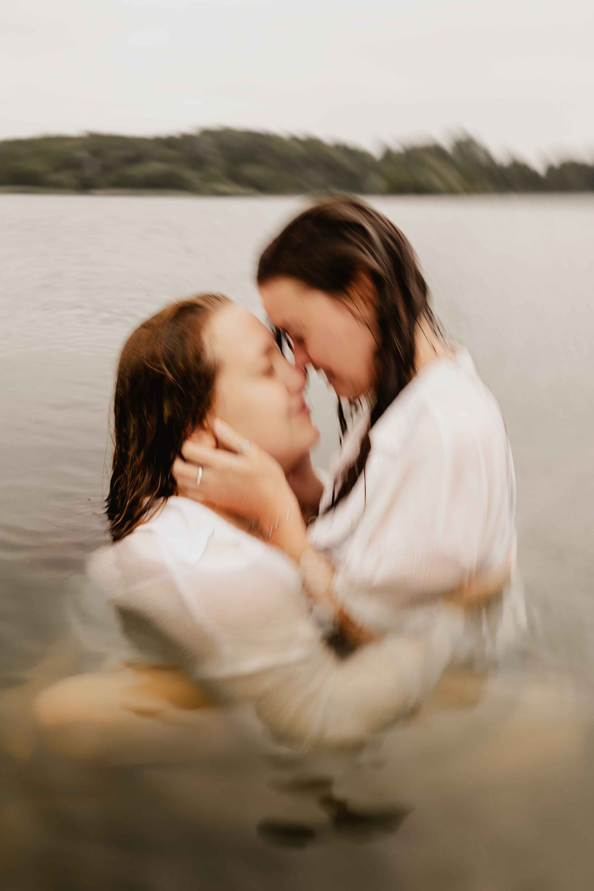 Zwei Frauen küssen sich liebevoll im See und halten sich dabei eng umschlungen