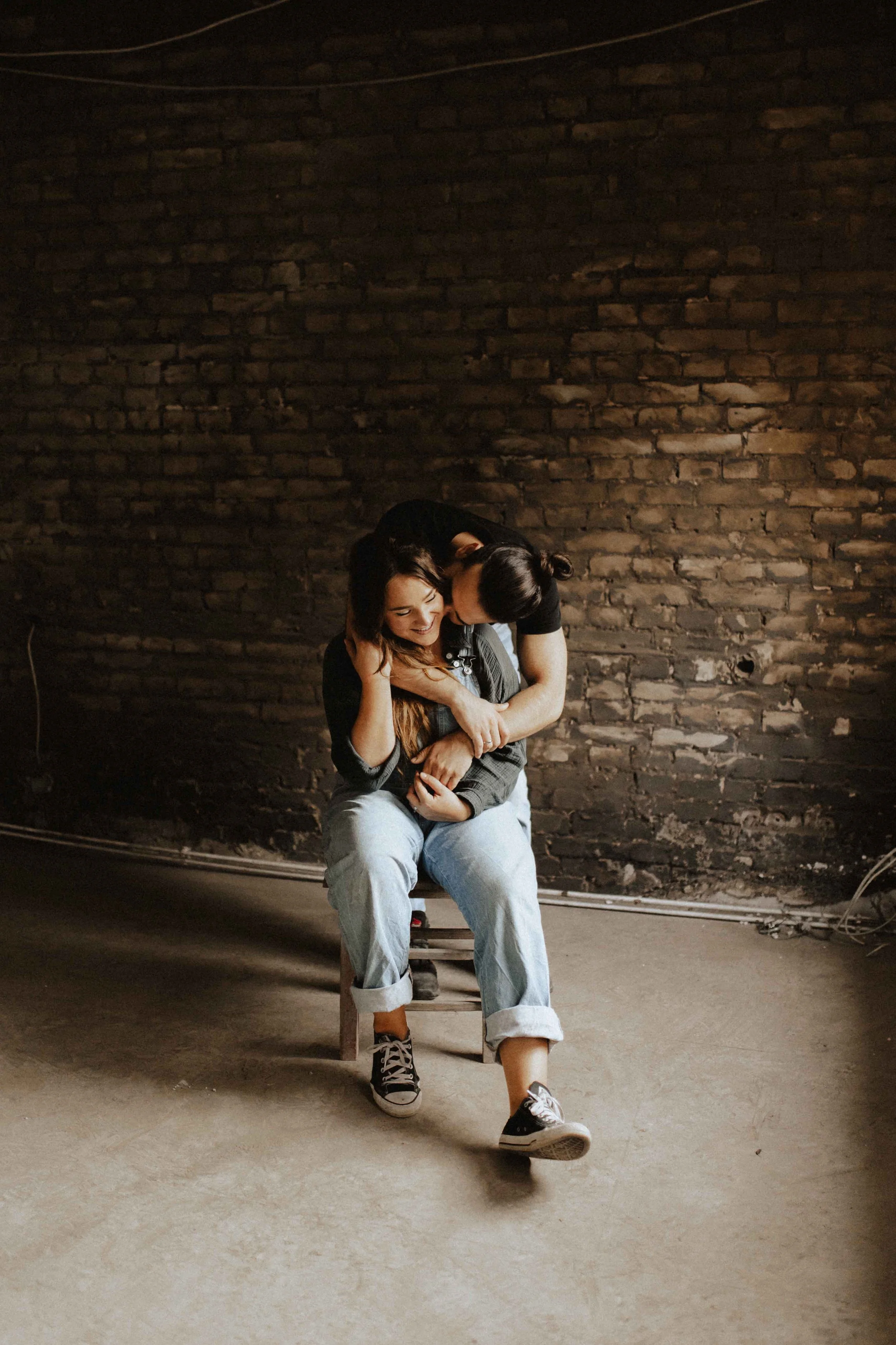Verliebtes Paar beim Paarshooting in Lüneburg – innige Umarmung auf einem Stuhl vor rustikaler Backsteinwand, authentische und gefühlvolle Paarfotografie.