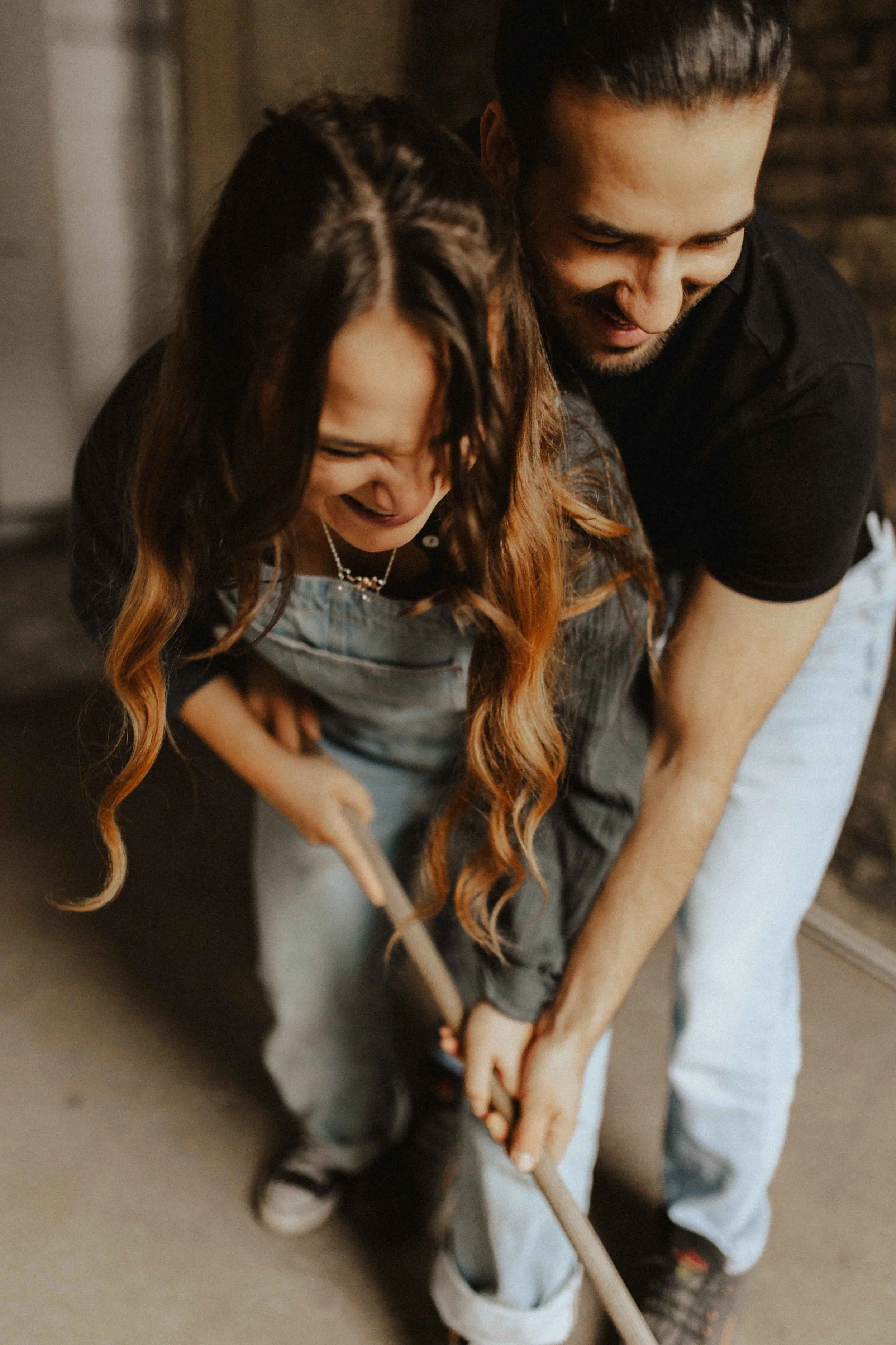 Paarshooting auf Baustelle – lachendes Paar fegt gemeinsam den Boden, Nahaufnahme der Gesichter und Hände in Lüneburg.