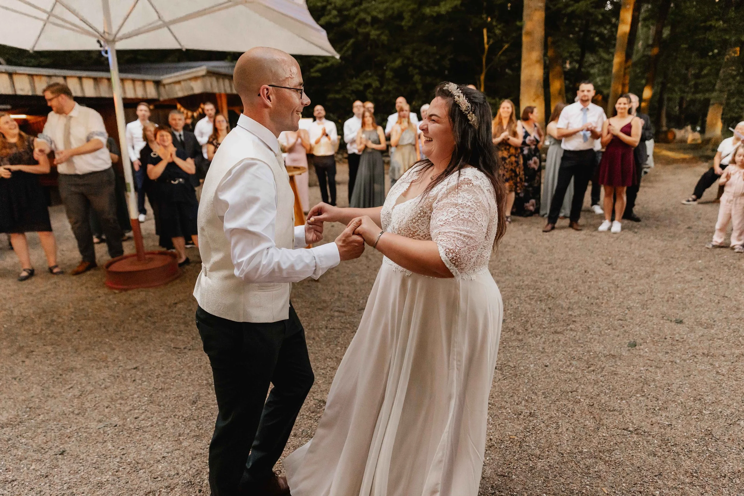 Braut und Bräutigam tanzen lachend den Hochzeitstanz im Freien vor den Gästen