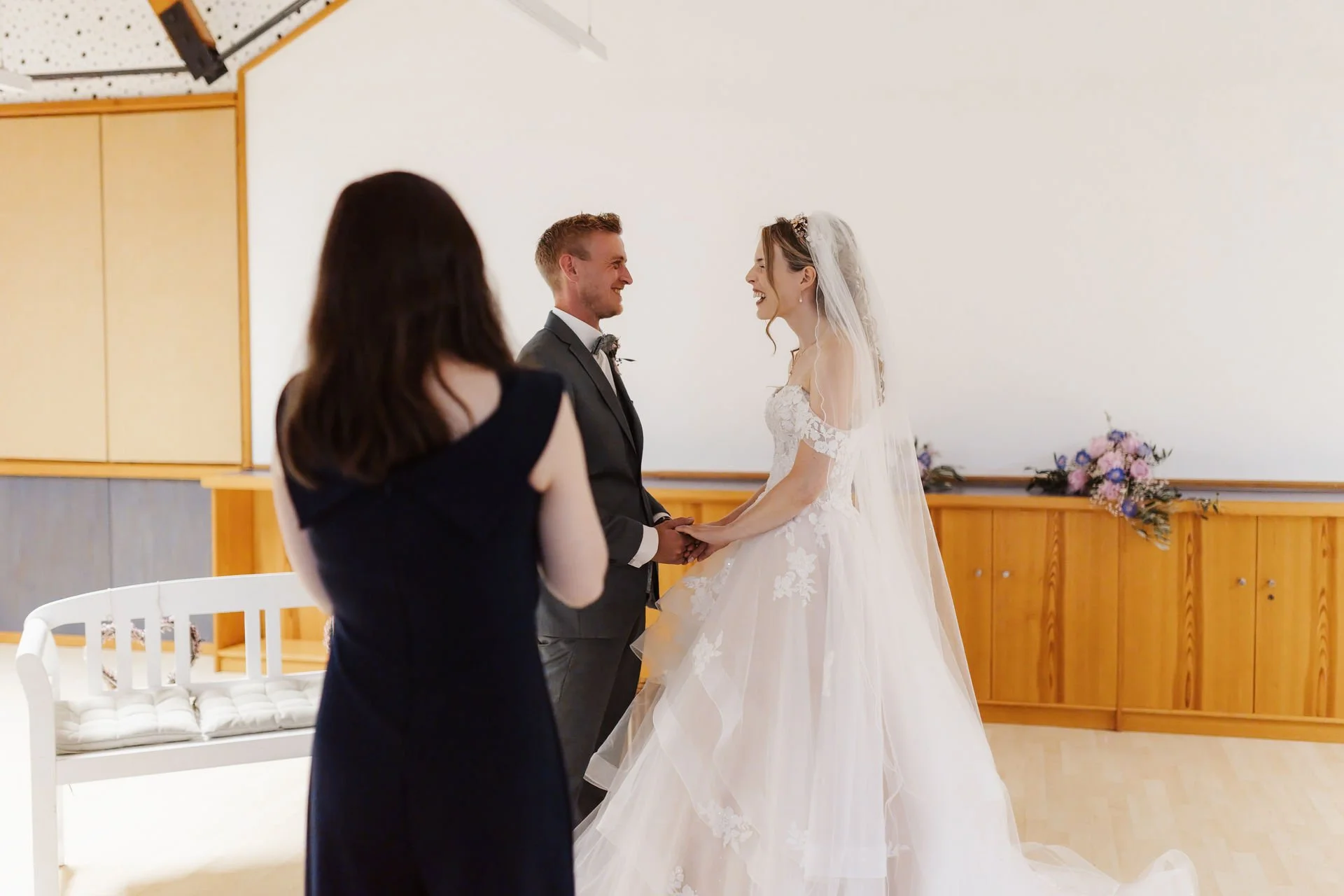 Glückliches Brautpaar hält sich während der freien Trauung im Heide Hotel Reinstorf bei Lüneburg an den Händen und lacht sich an. Ein authentischer Moment der Hochzeitsreportage mit Traurednerin im Vordergrund.