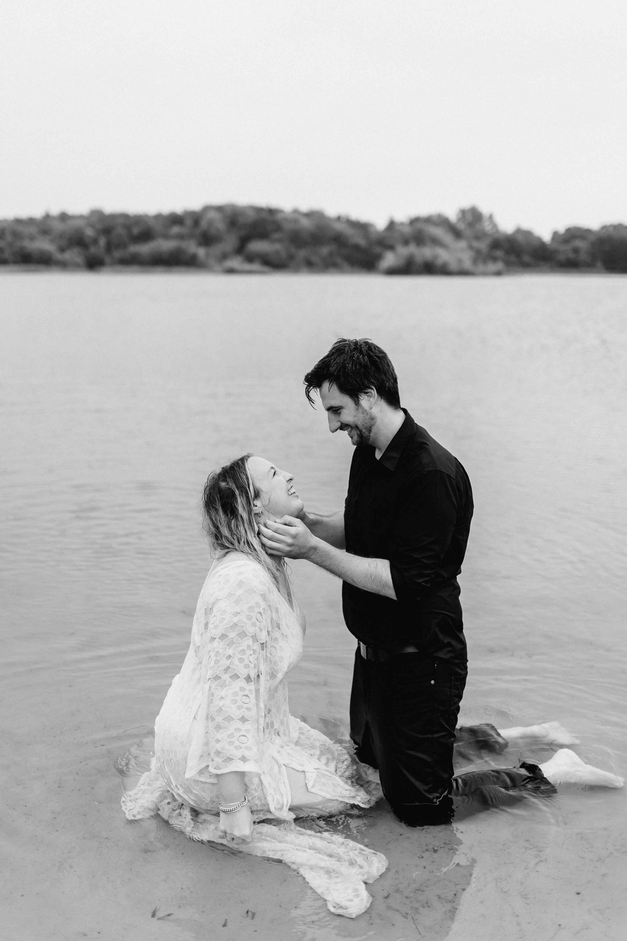 Paar kniet sich im Wasser gegenüber, er berührt sanft ihr Gesicht und beide lächeln