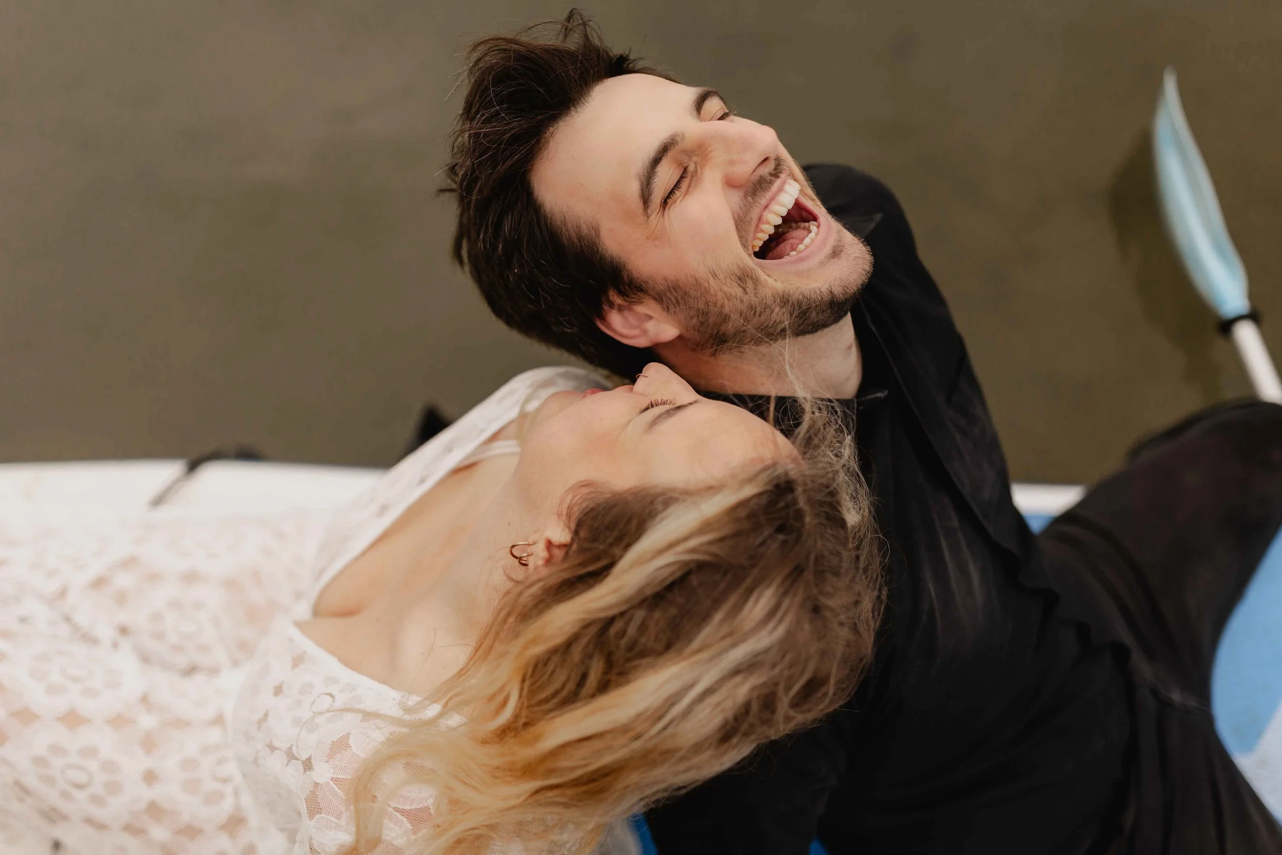 Paar liegt lachend auf einem SUP-Board am See und genießt den Moment voller Lebensfreude