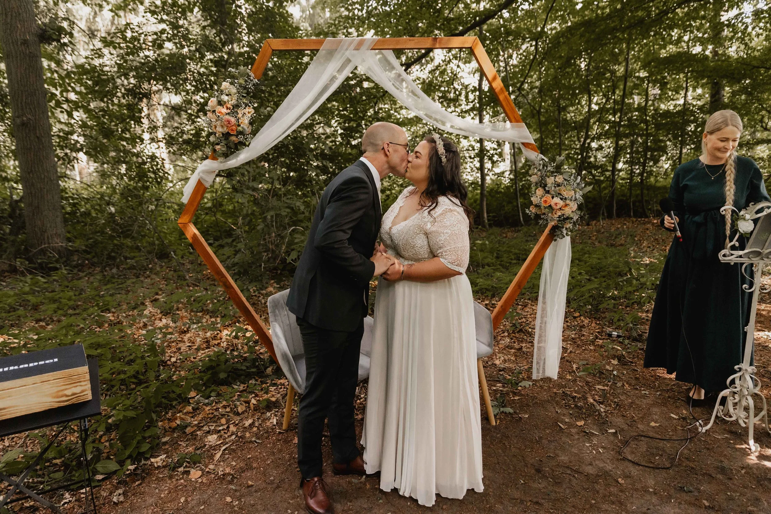 Hochzeitspaar küsst sich nach dem Eheversprechen vor dem Blumenbogen im Wald