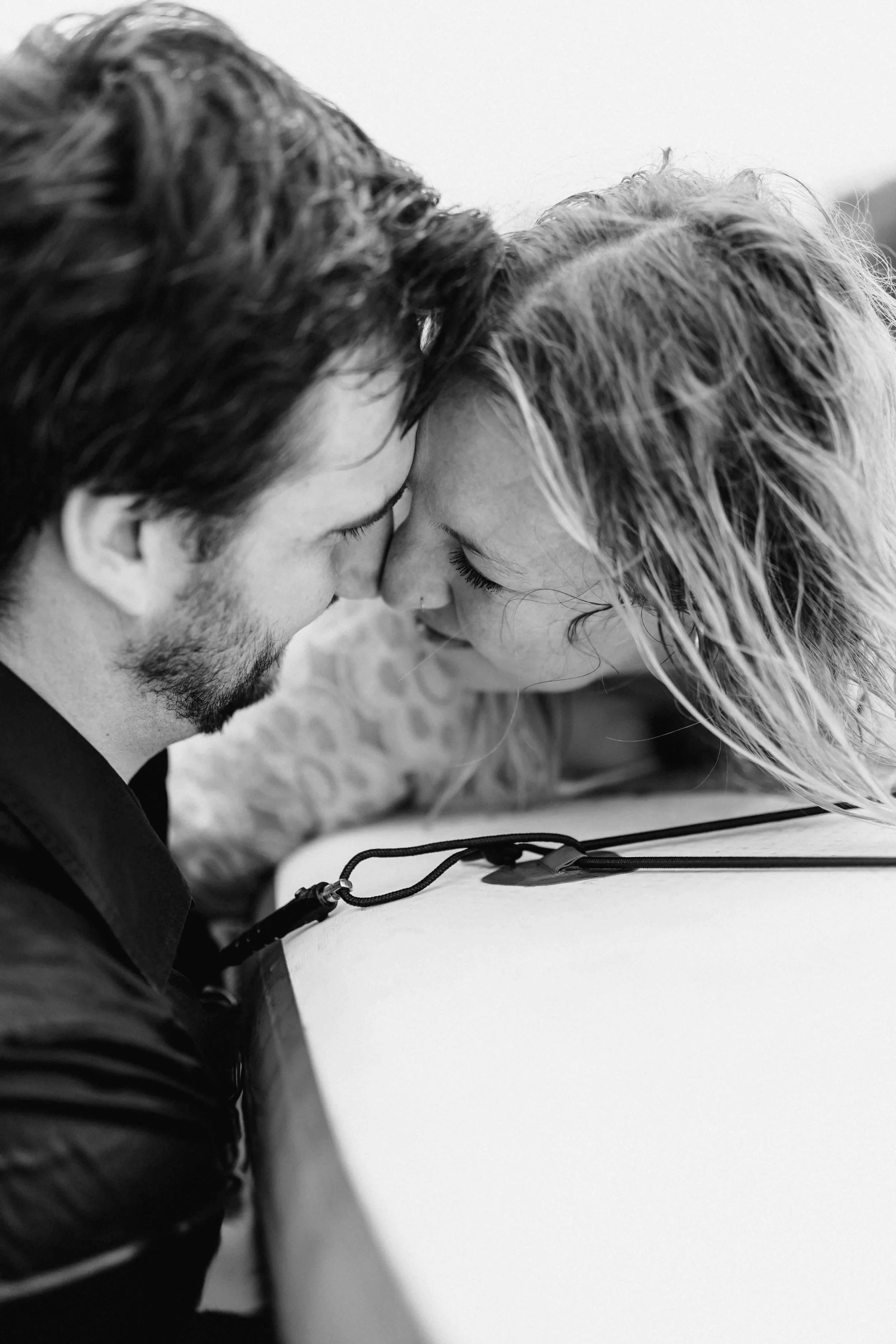 Paar liegt eng beieinander auf einem SUP-Board, Stirn an Stirn mit zärtlichem Lächeln in Schwarz-Weiß