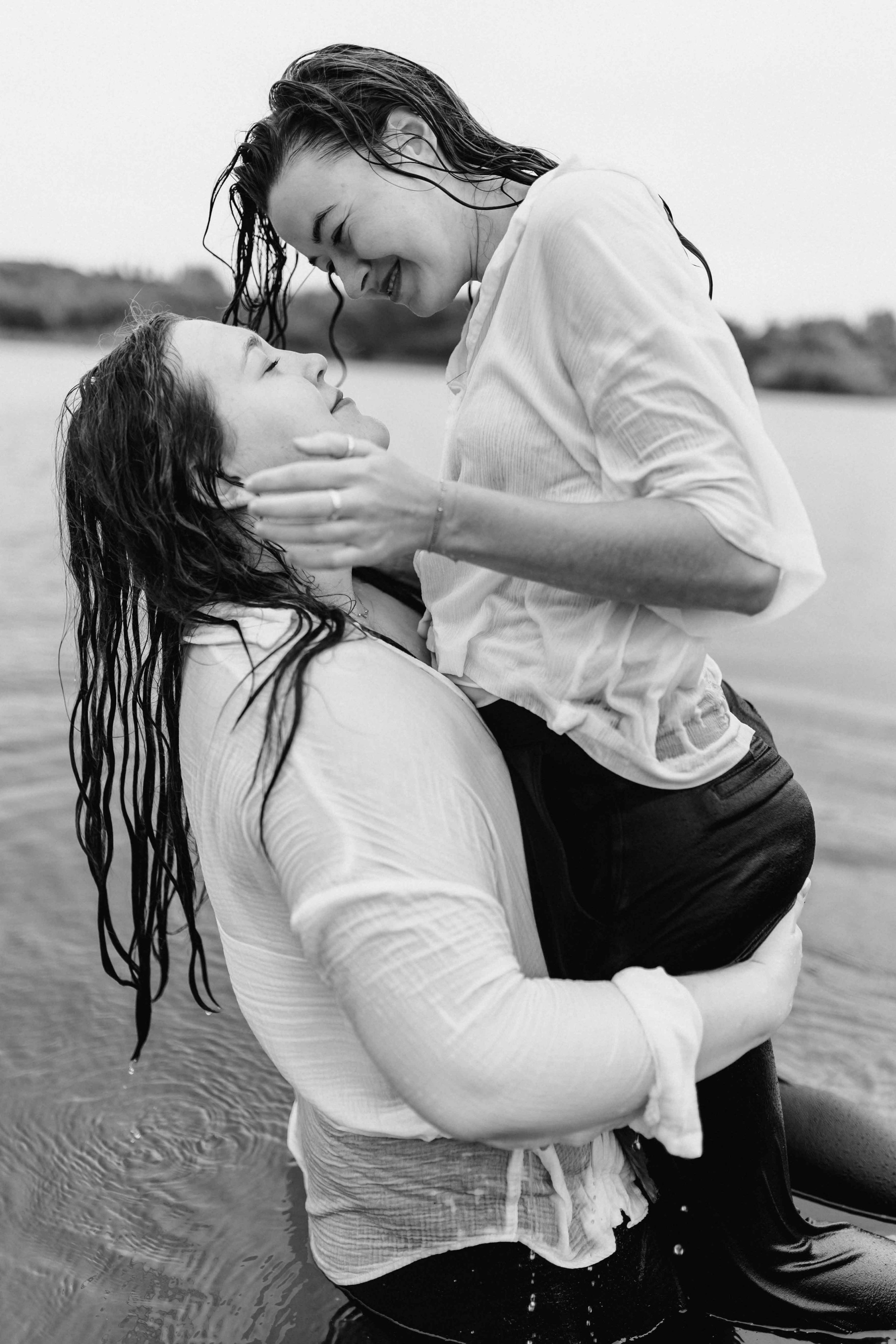 Zwei Frauen im Wasser, eine hebt die andere lachend hoch, Schwarz-Weiß-Aufnahme voller Lebensfreude