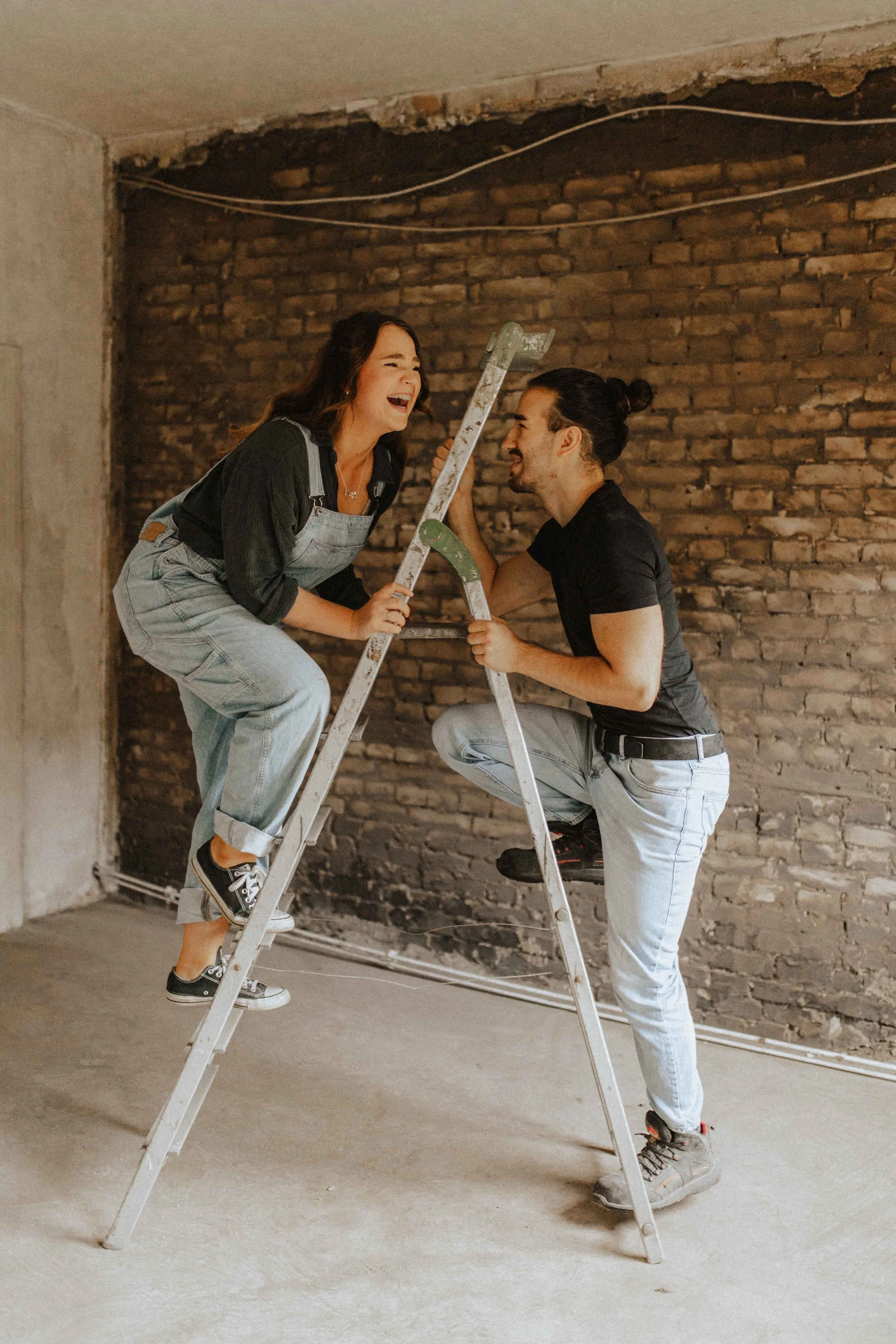 Paarshooting in Uelzen – lachendes Paar steht spielerisch an einer Leiter in einem Raum mit Backsteinwand.