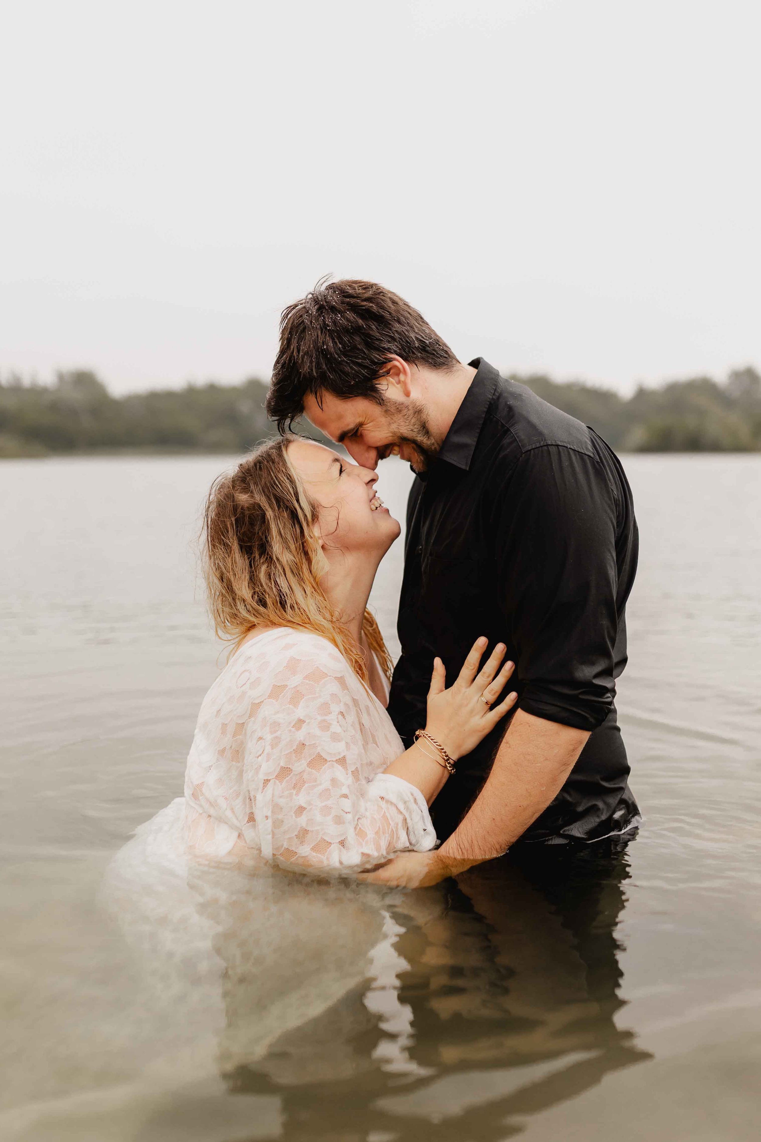 Paar steht umarmt im Wasser, Stirn an Stirn und lächelt sich zärtlich an
