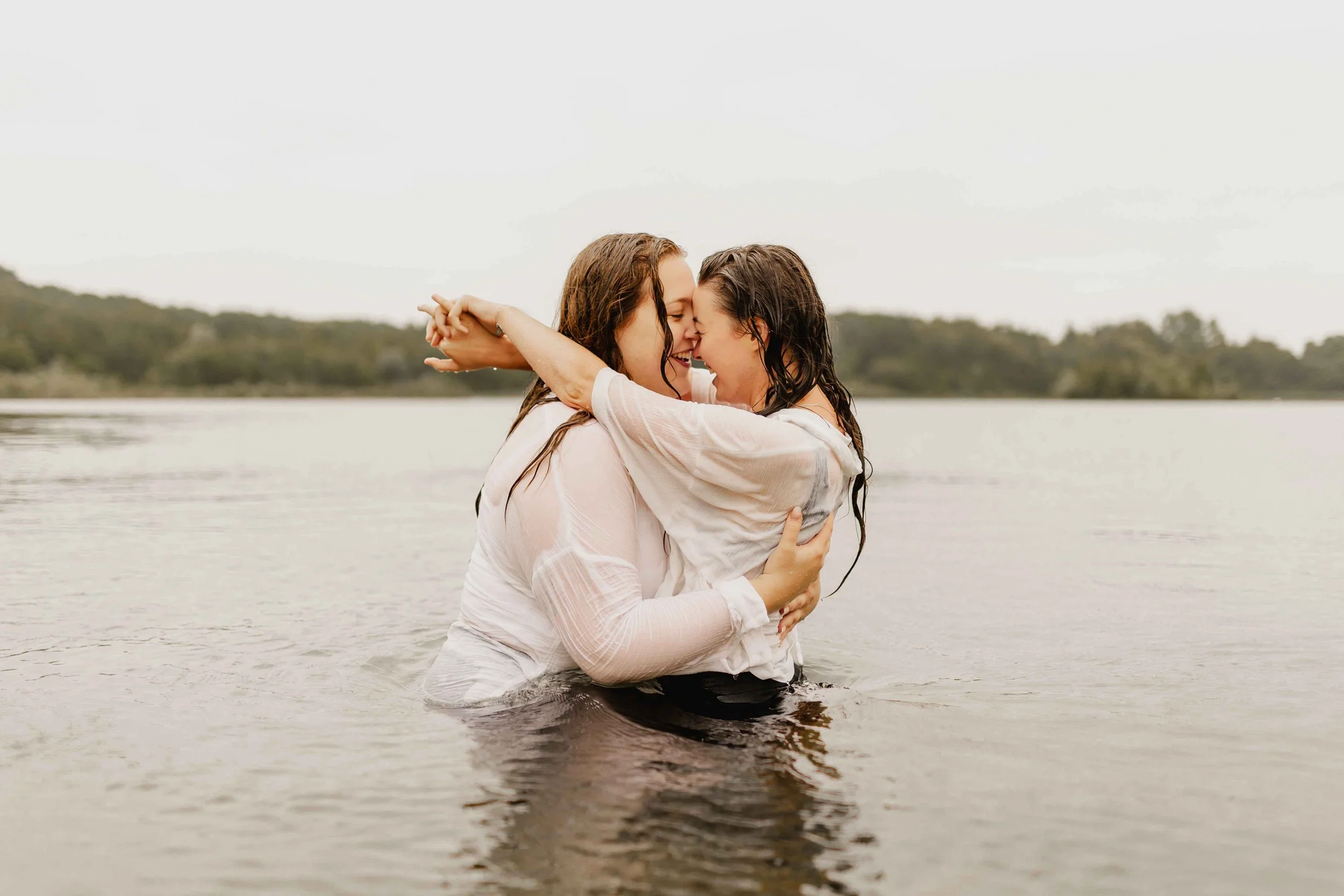 Zwei Frauen umarmen sich eng im See und schauen sich verliebt an, Paarshooting im Wasser