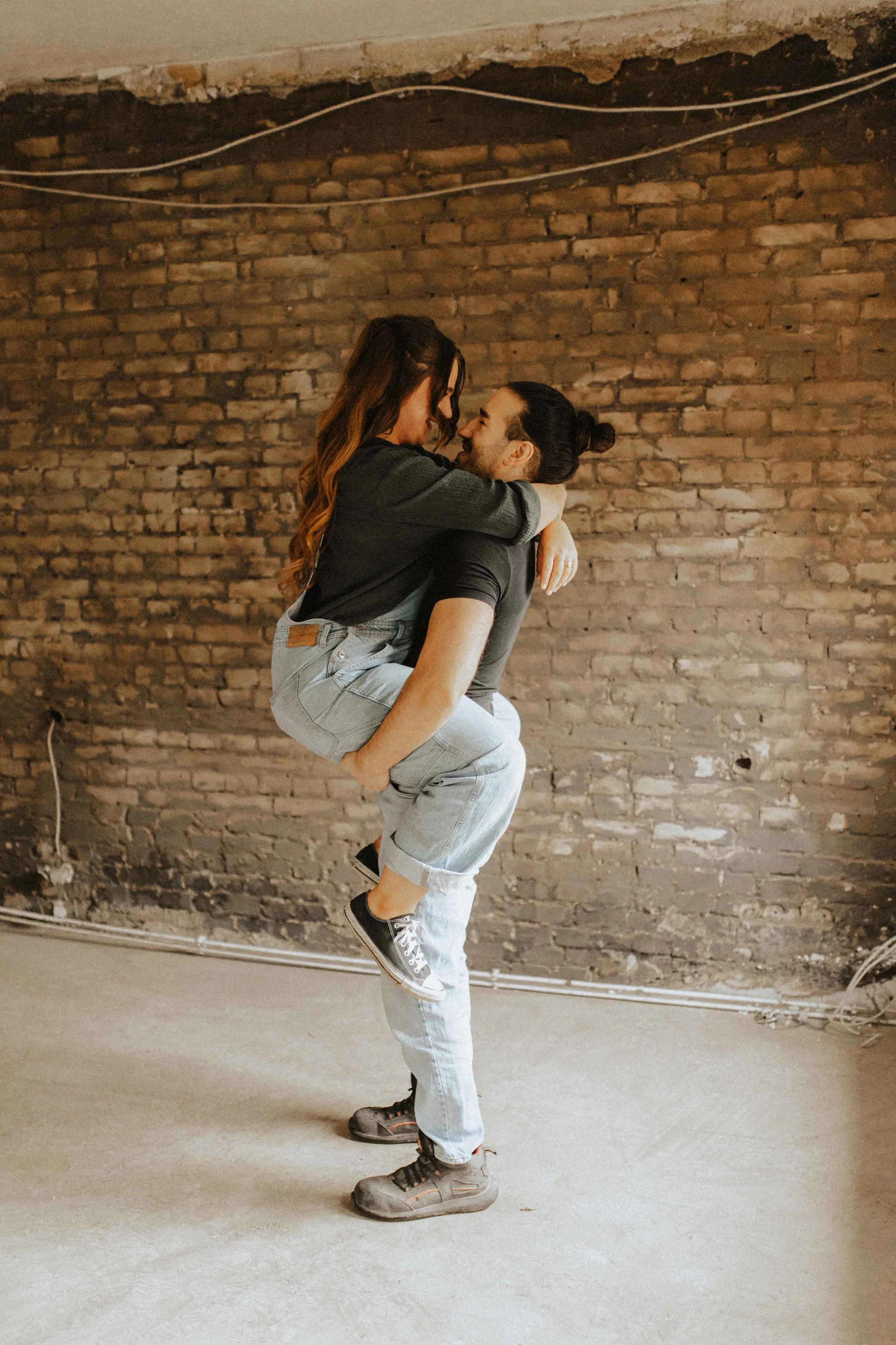 Romantisches Paarshooting auf Baustelle – Frau umarmt Mann sprungartig vor Backsteinwand in Lüneburg.