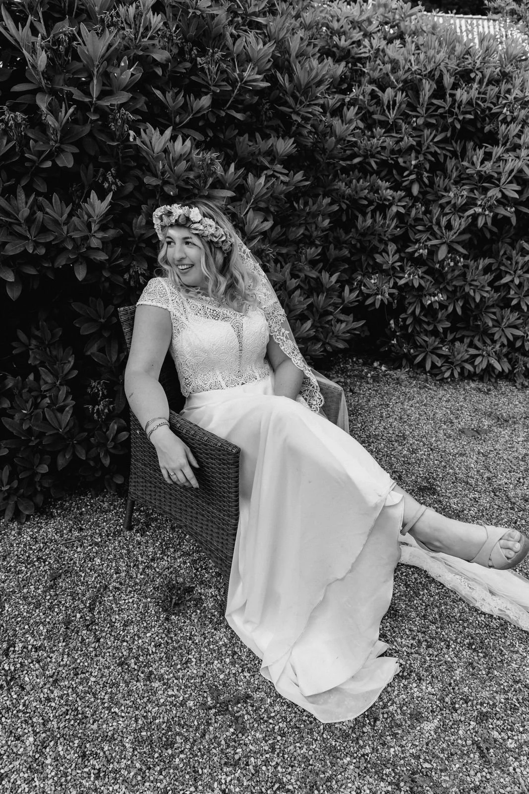 Entspannte Braut sitzt im Hochzeitskleid auf einer Bank im Garten in Lüneburg in schwarz-weiß