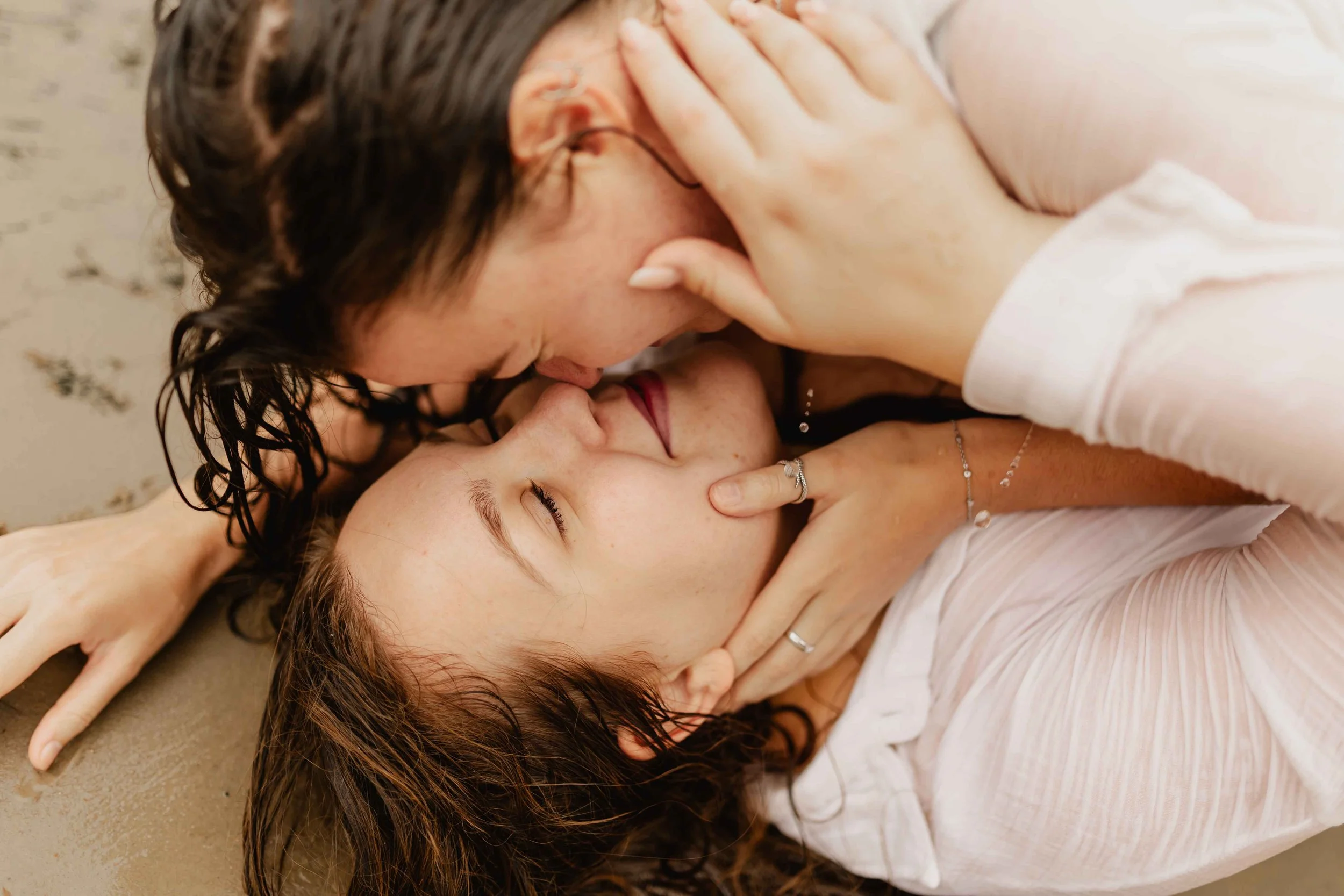 Zwei Frauen liegen eng umschlungen am Ufer im Wasser und küssen sich leidenschaftlich