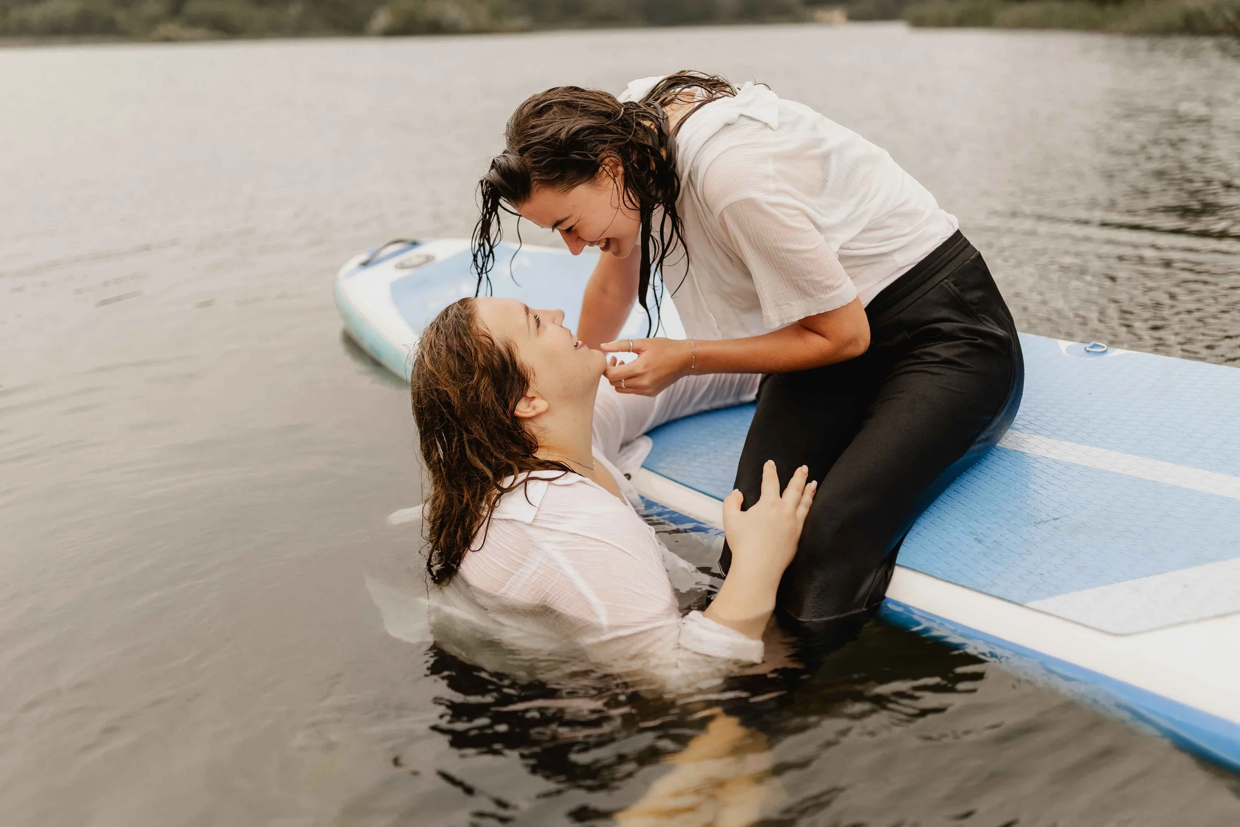 Romantischer Moment zweier Frauen – eine sitzt auf dem SUP, die andere im Wasser, beide sehen sich verliebt an