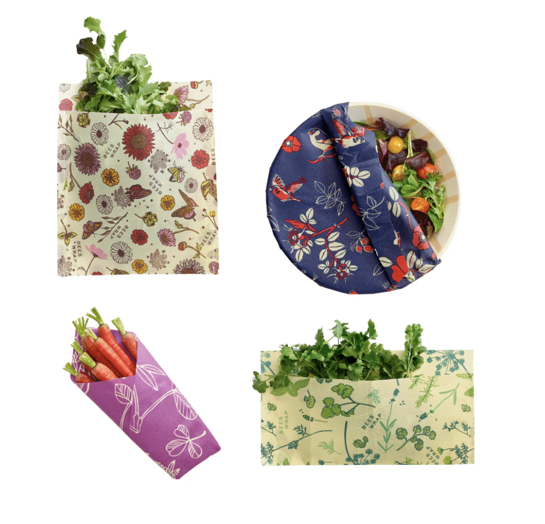 Reusable fabric wraps with different patterns covering fresh vegetables and a bowl of salad.
