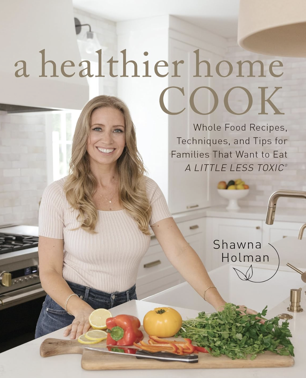 A woman in a kitchen with vegetables on a cutting board, featured on the cover of "A Healthier Home Cook" cookbook by Shawna Holman. The text highlights whole food recipes and tips for less toxic eating.