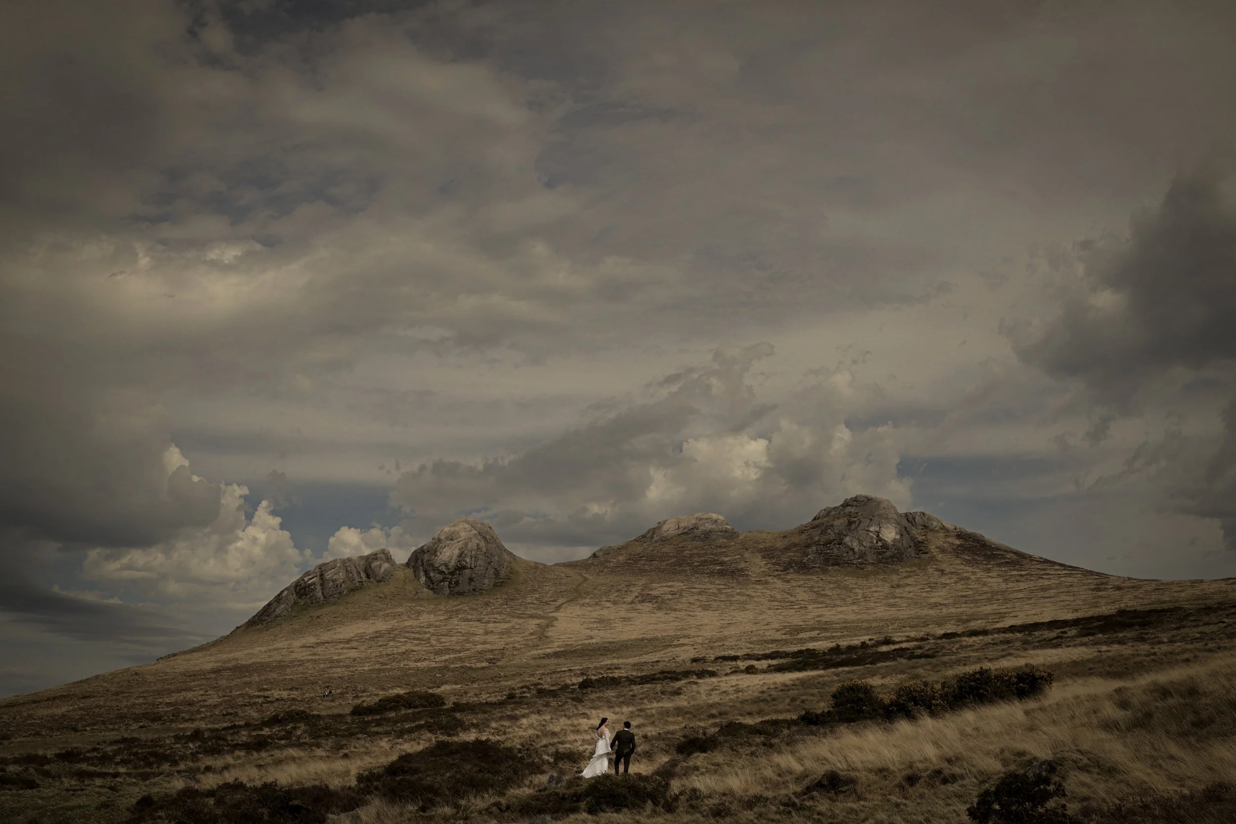 A elope couple standing hand in hand on a irish grassy hillside with large rocky hills in the background under a cloudy sky at the Mourne Mountains.