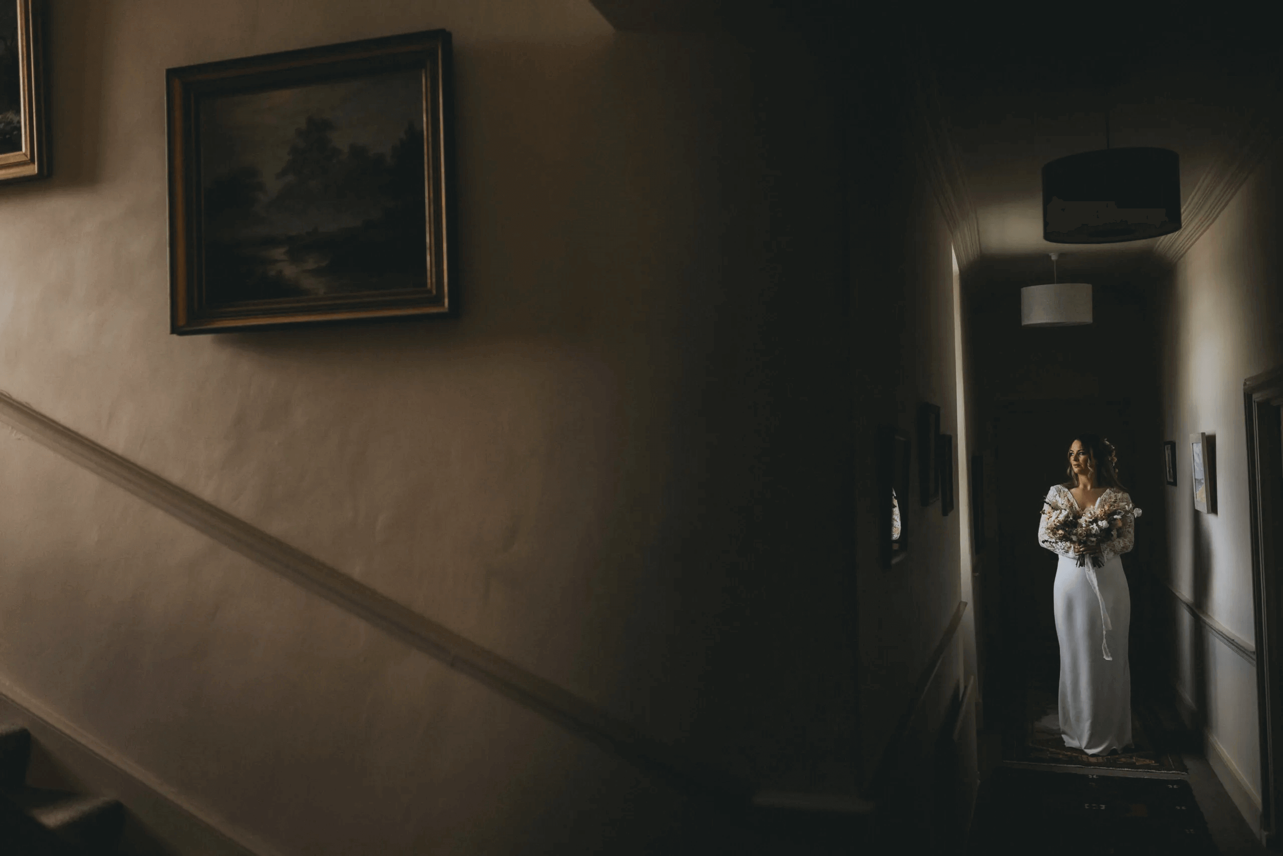 A bride in a white dress holding a bouquet, standing in a dimly lit hallway at Cloughjordan House during an elopement.