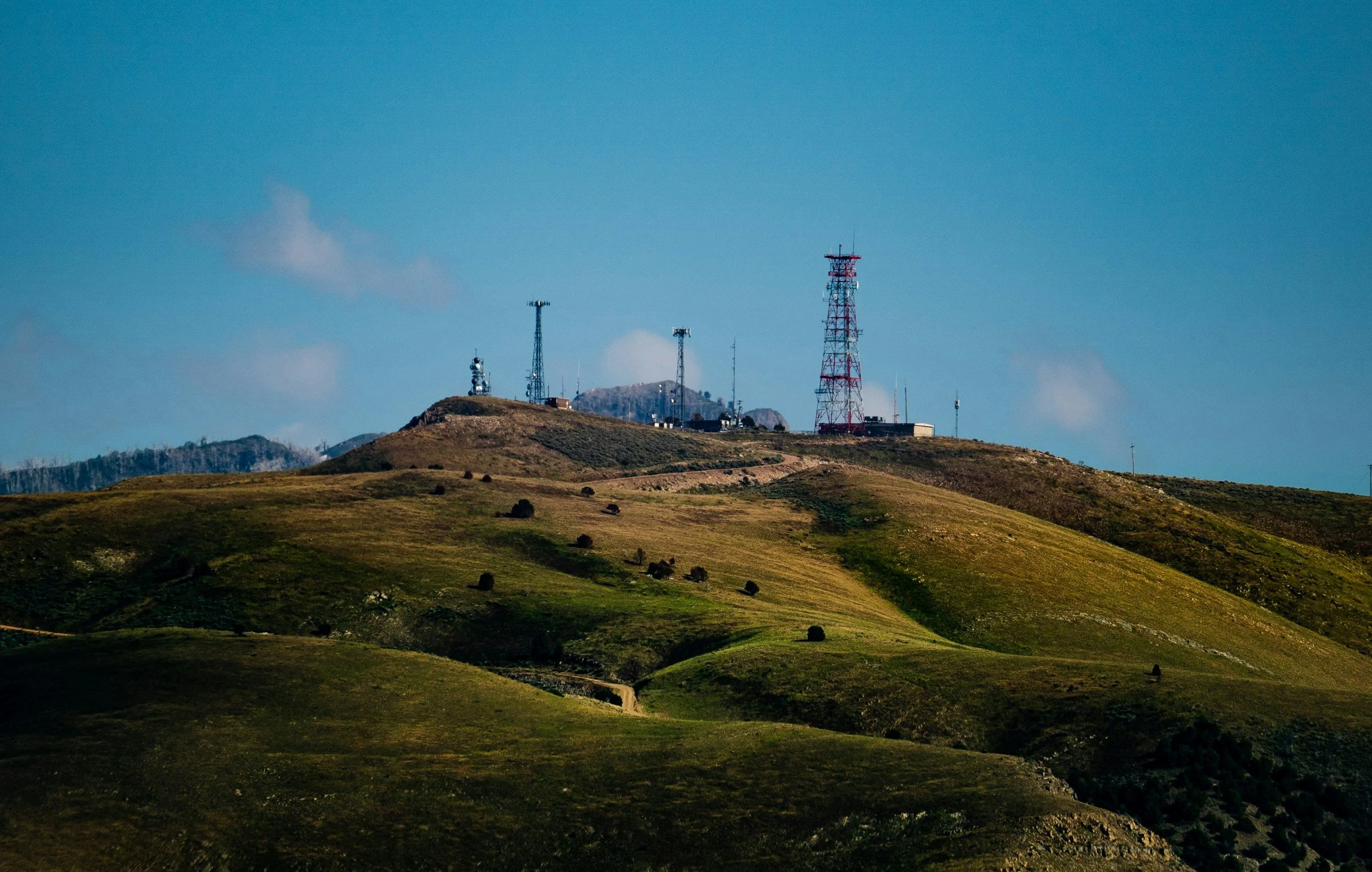 Hilly Michigan landscape with communication towers and antennas on the hilltop, under a clear blue sky.