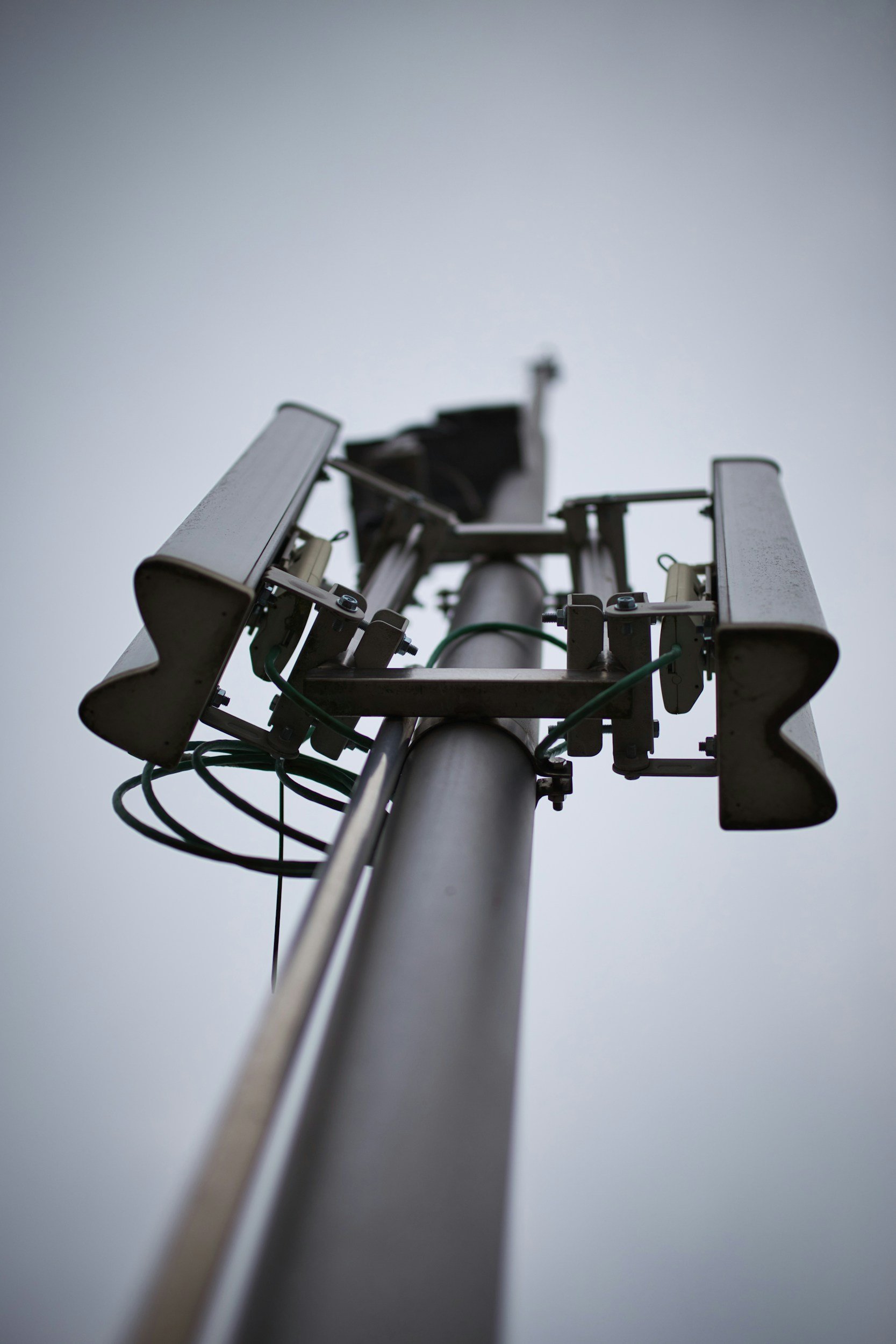 Close-up of a cellular telephone tower antenna array mounted on top of a metal pole against a gray sky.