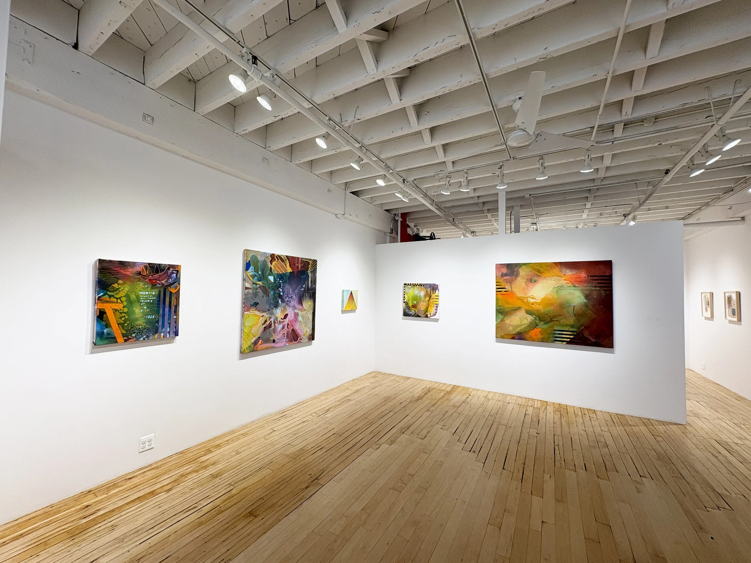 An art gallery with colorful abstract paintings on white walls and a wooden floor, under a ceiling with white beams and track lighting.