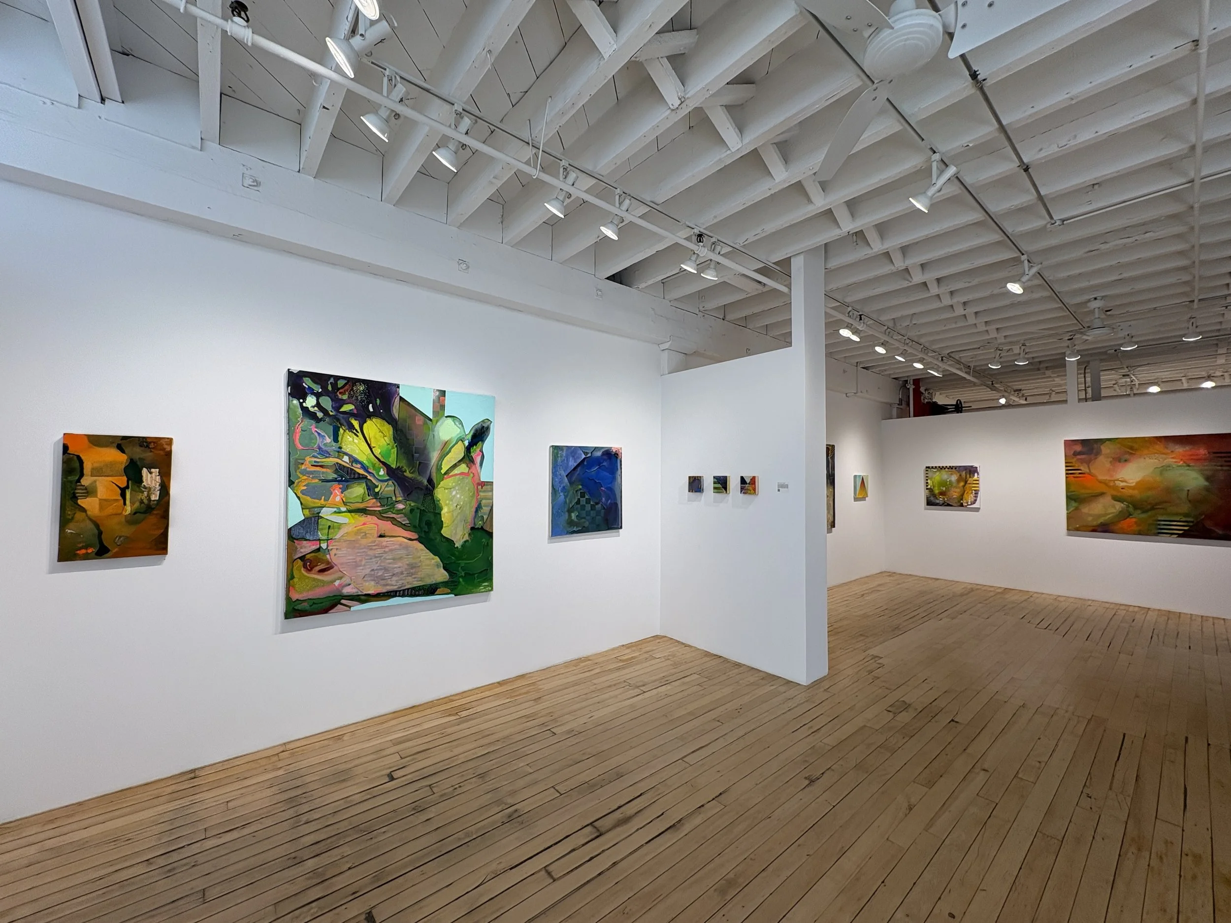 Interior of an art gallery with white walls and wooden floors, displaying colorful abstract paintings.