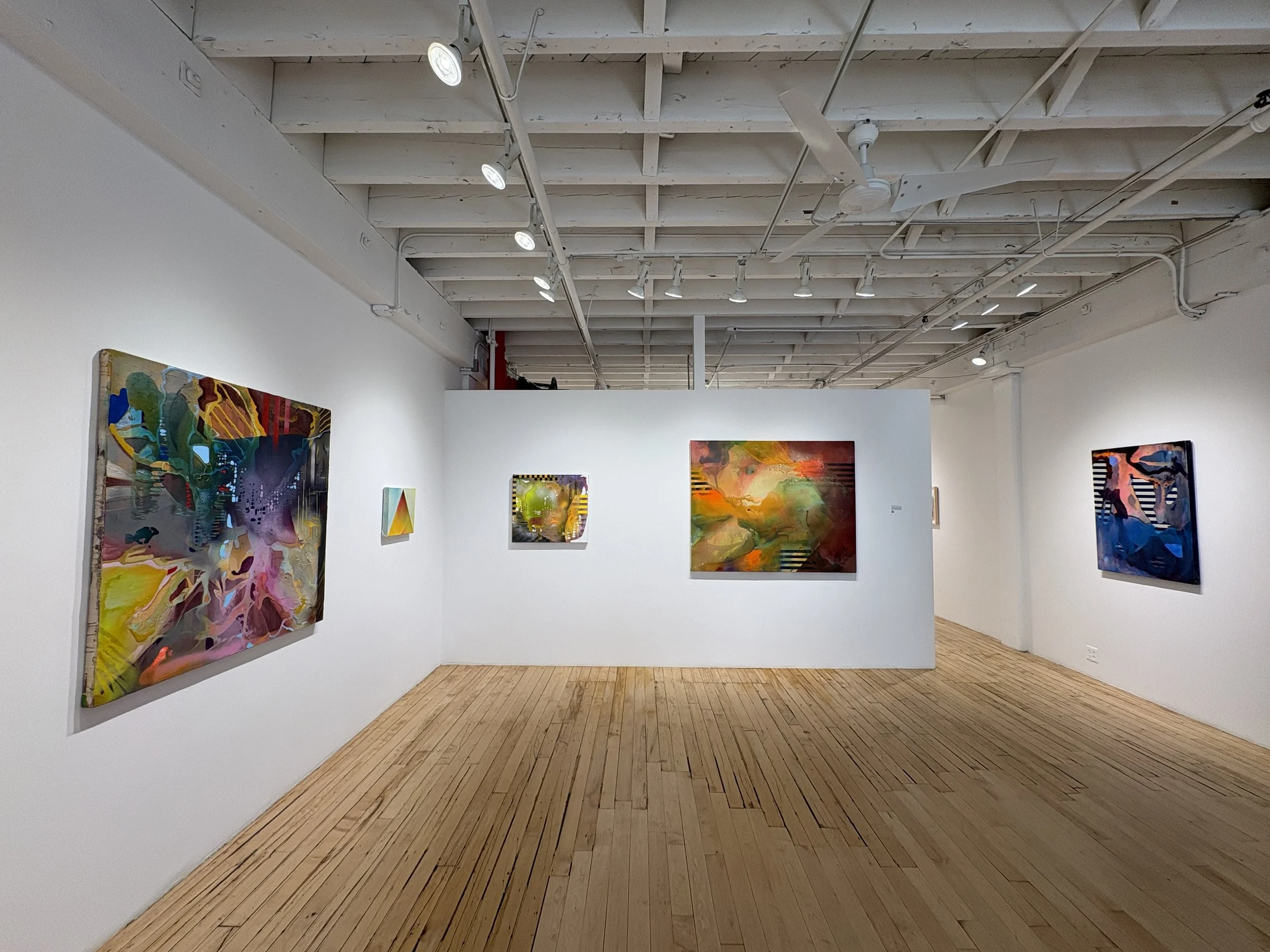 Gallery with colorful abstract paintings on white walls, hardwood floor, ceiling with track lighting, and visible ductwork.