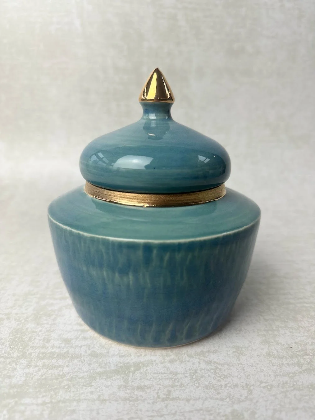Blue ceramic jar with a gold-tipped lid on a textured surface.