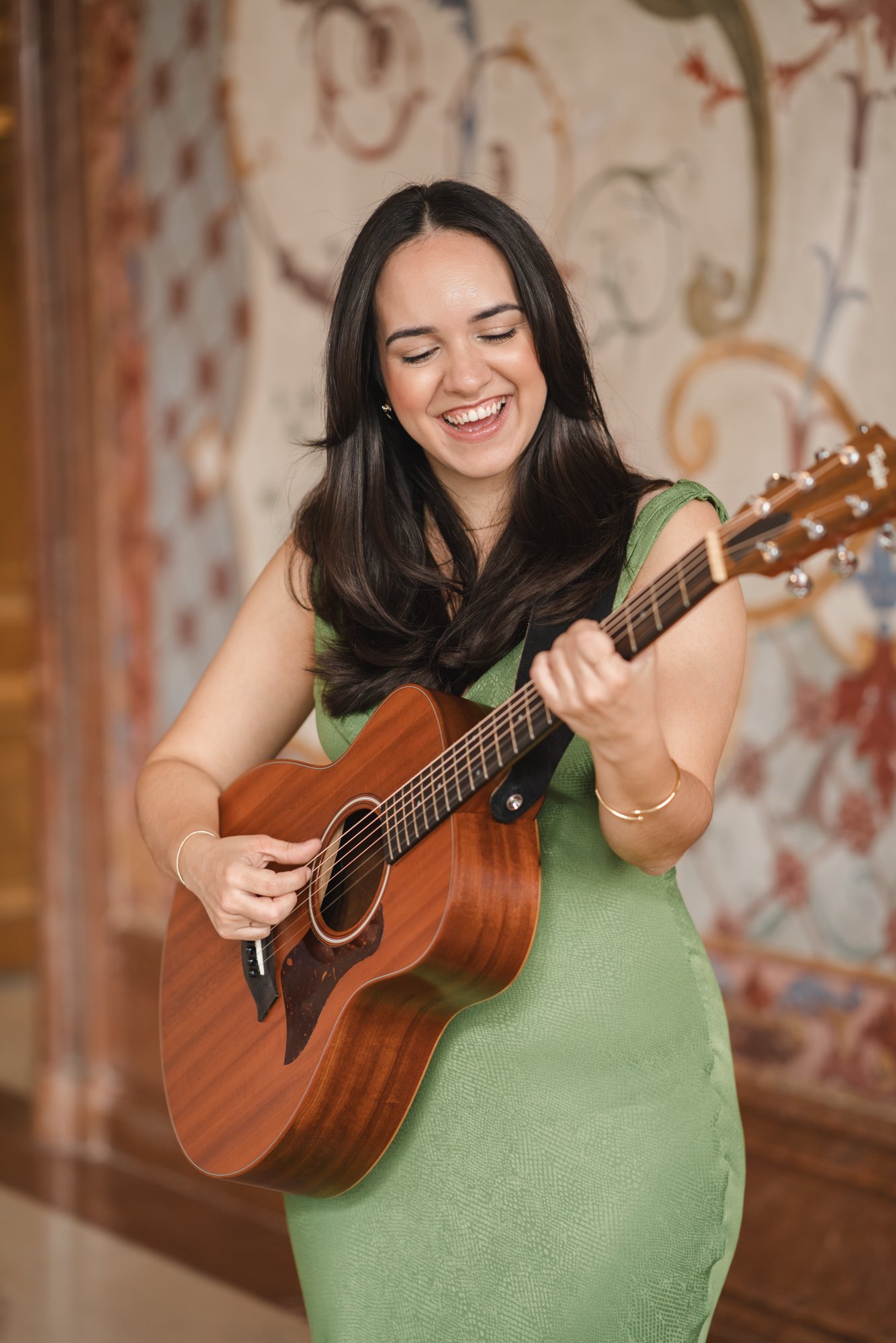 Eine Frau in einem grünen Kleid spielt eine akustische Gitarre und lächelt.