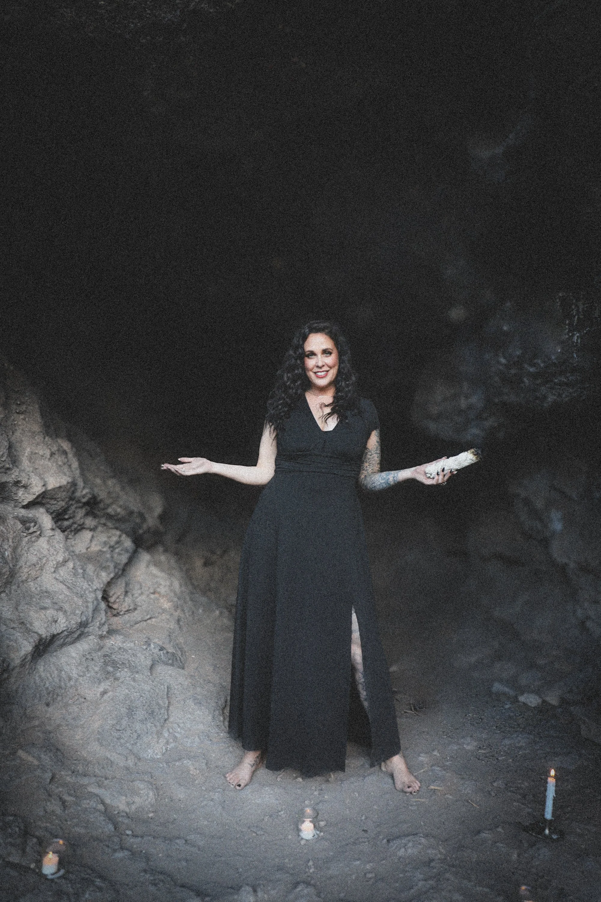 Woman in a black dress standing barefoot before a rock face, arms open