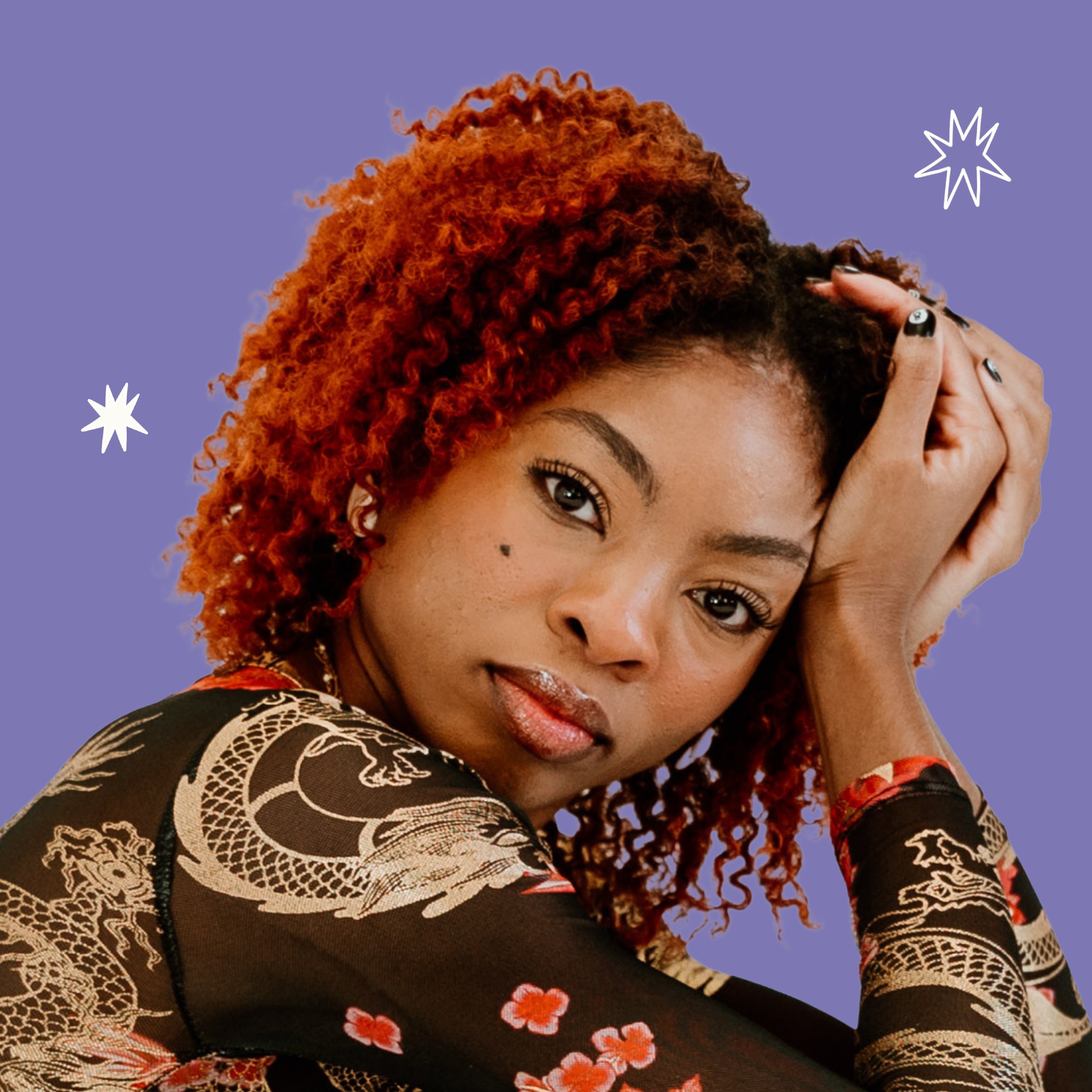 A woman with curly red hair, wearing a black dress with floral patterns and lace detailing, posing against a purple background with white starburst designs.