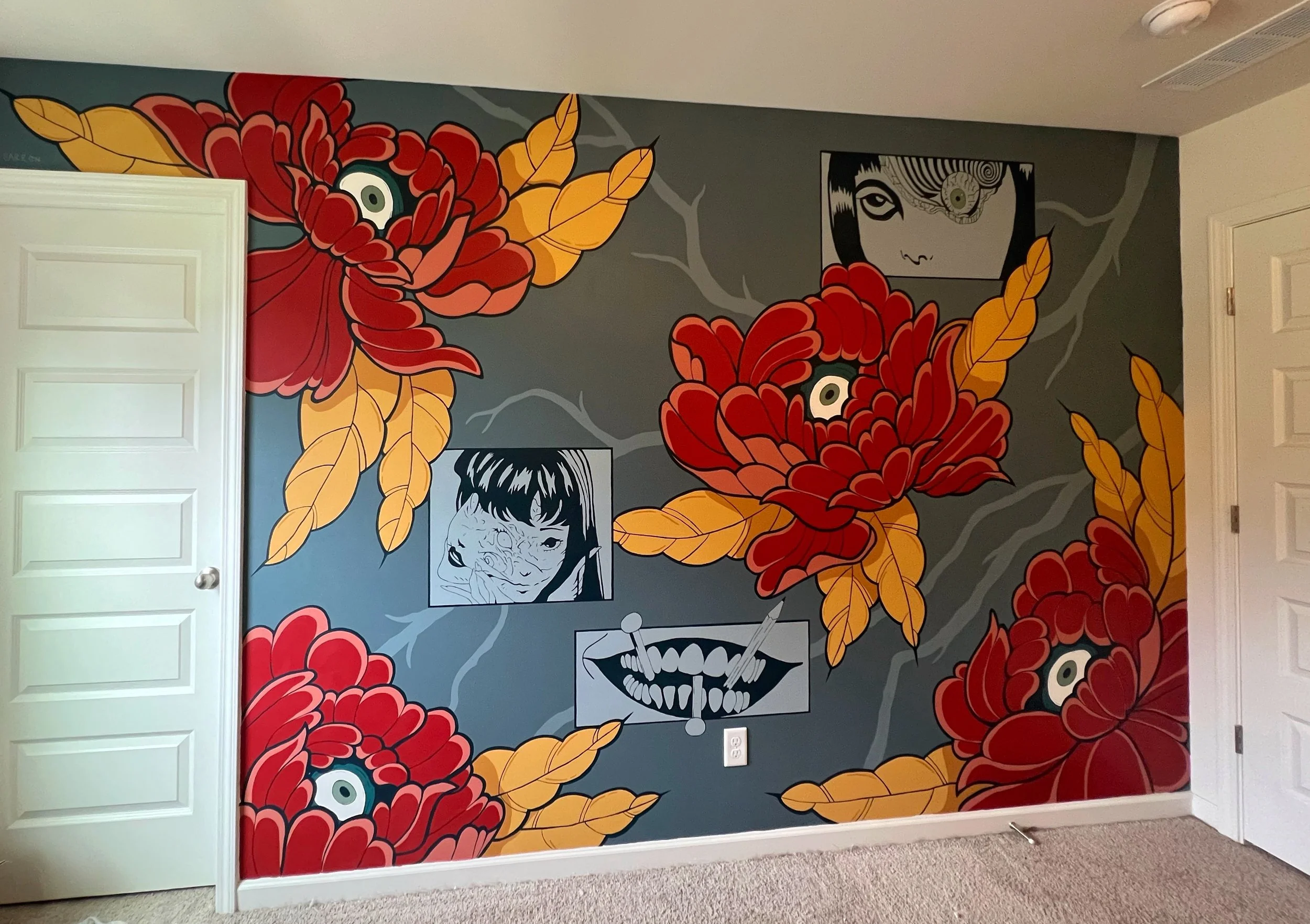 A colorful mural featuring large red and orange flowers with yellow leaves, black and white illustrated faces, and abstract patterns on a dark gray wall in a room.