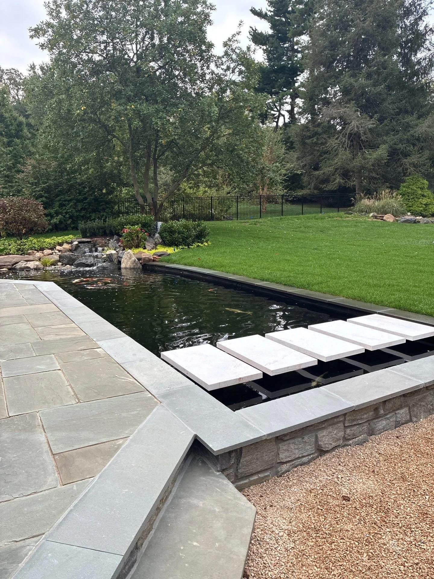 Large traditional koi pond with manicured stone edges and floating steps in Lower Merion Township, PA