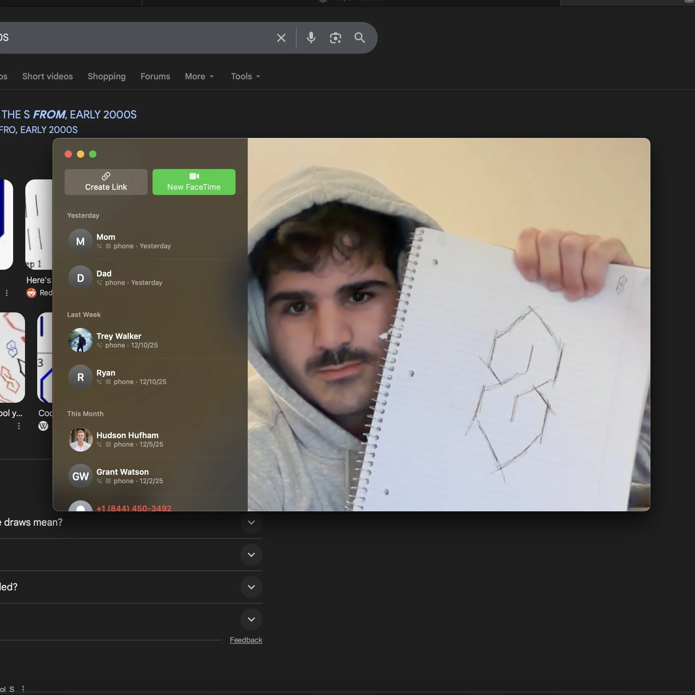 A young man with dark hair and facial hair is wearing a white hoodie with the hood up and holding a spiral notebook foreshortening towards the camera. The notebook shows a sketch of a three-dimensional geometric shape resembling a cube or wireframe figure.