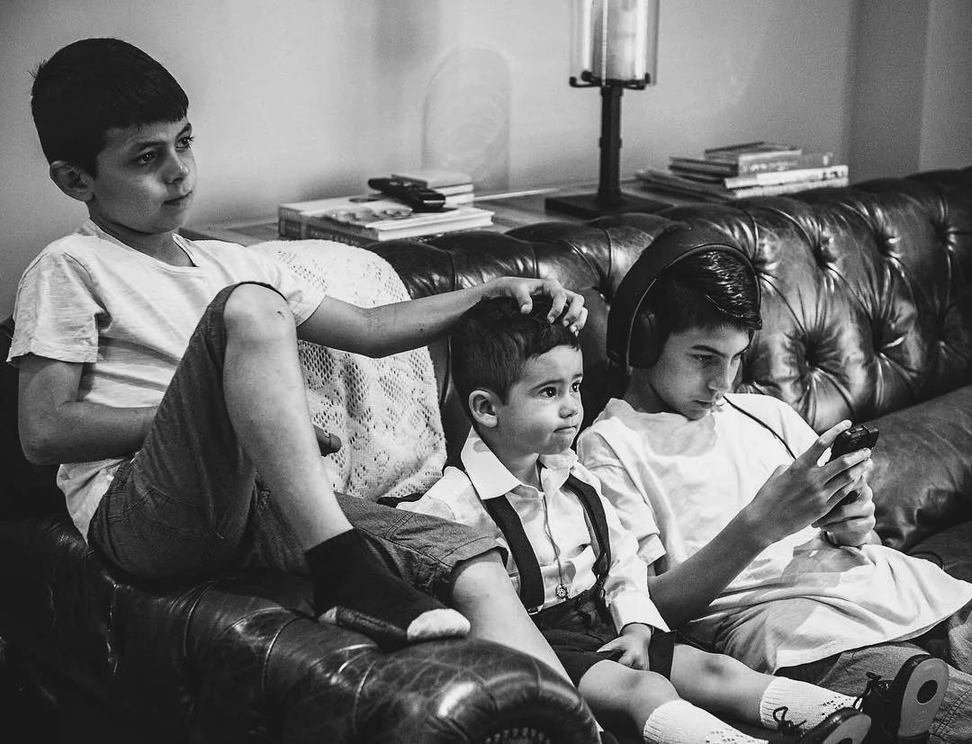 A documentary style black and white photo of 3 brothers hanging out with each other on the family room couch