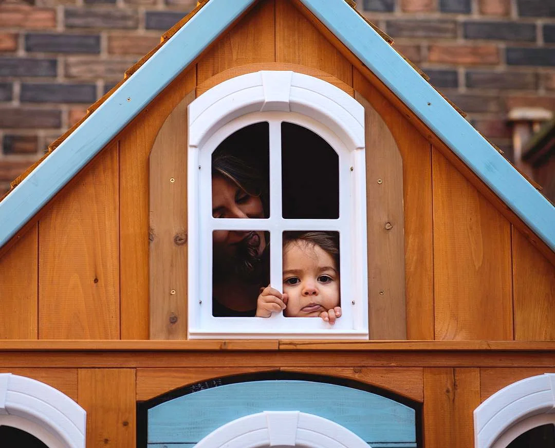 A mother and her young daughter playing in their backyard playhouse