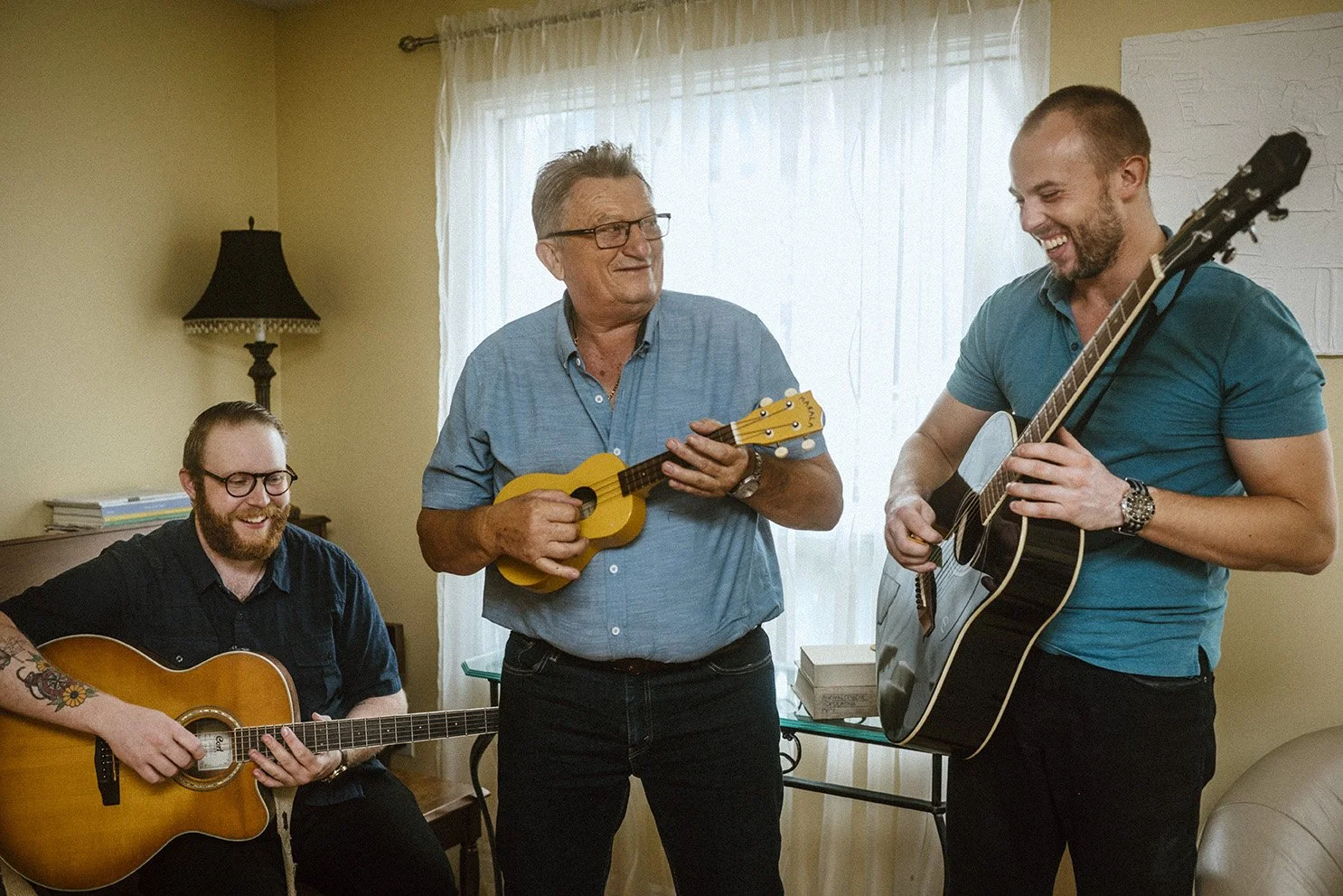 Father and two adult sons playing guitars and singing together in a cozy room, smiling and enjoying a musical jam session.