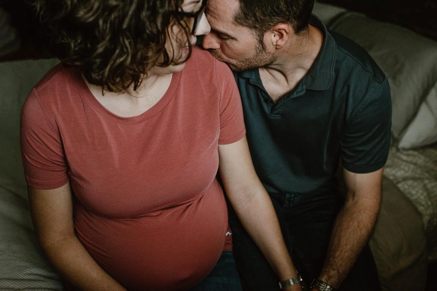 A pregnant woman and a man sharing an intimate moment, with their foreheads touching and eyes closed.