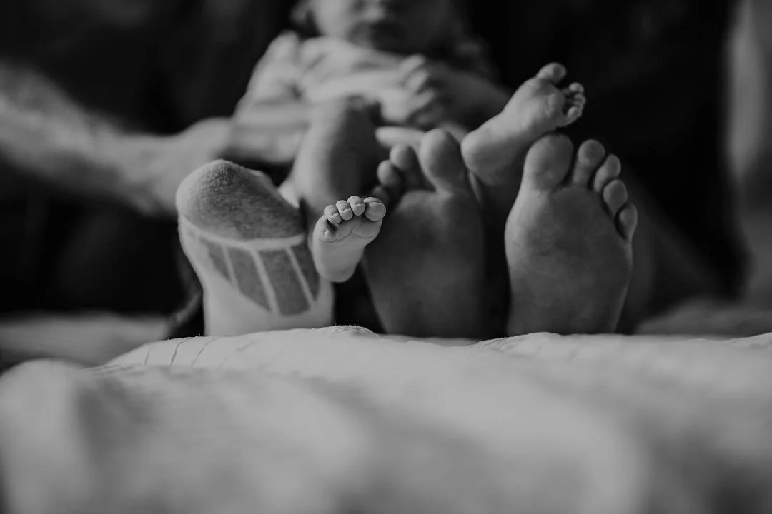 Close-up of the tiny feet of a newborn baby lying on a bed, with the focus on the soles and toes, in black and white.