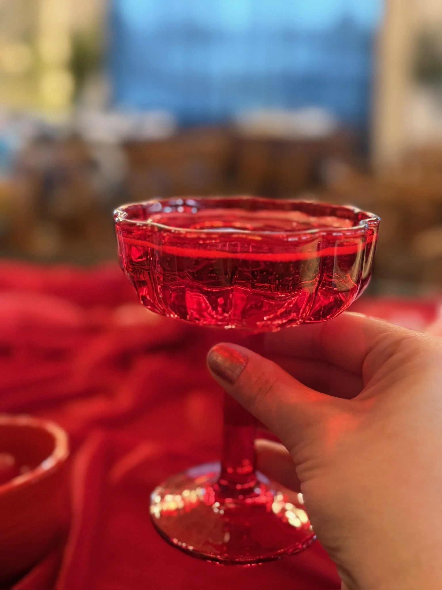 A person holding a red glass dessert cup with a short stem, filled with a red jelly or gelatin dessert, against a blurred background.