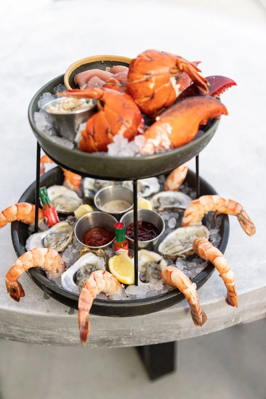 Seafood platter with lobster, shrimp, oysters on ice, lemon wedges, and dipping sauces.