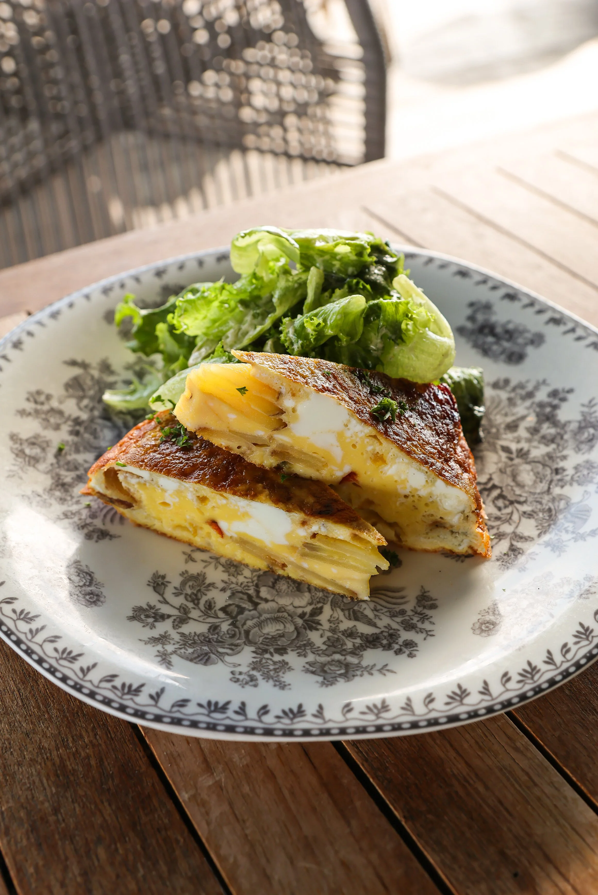 A plate with a slice of potato frittata and a side of green salad on a wooden table.