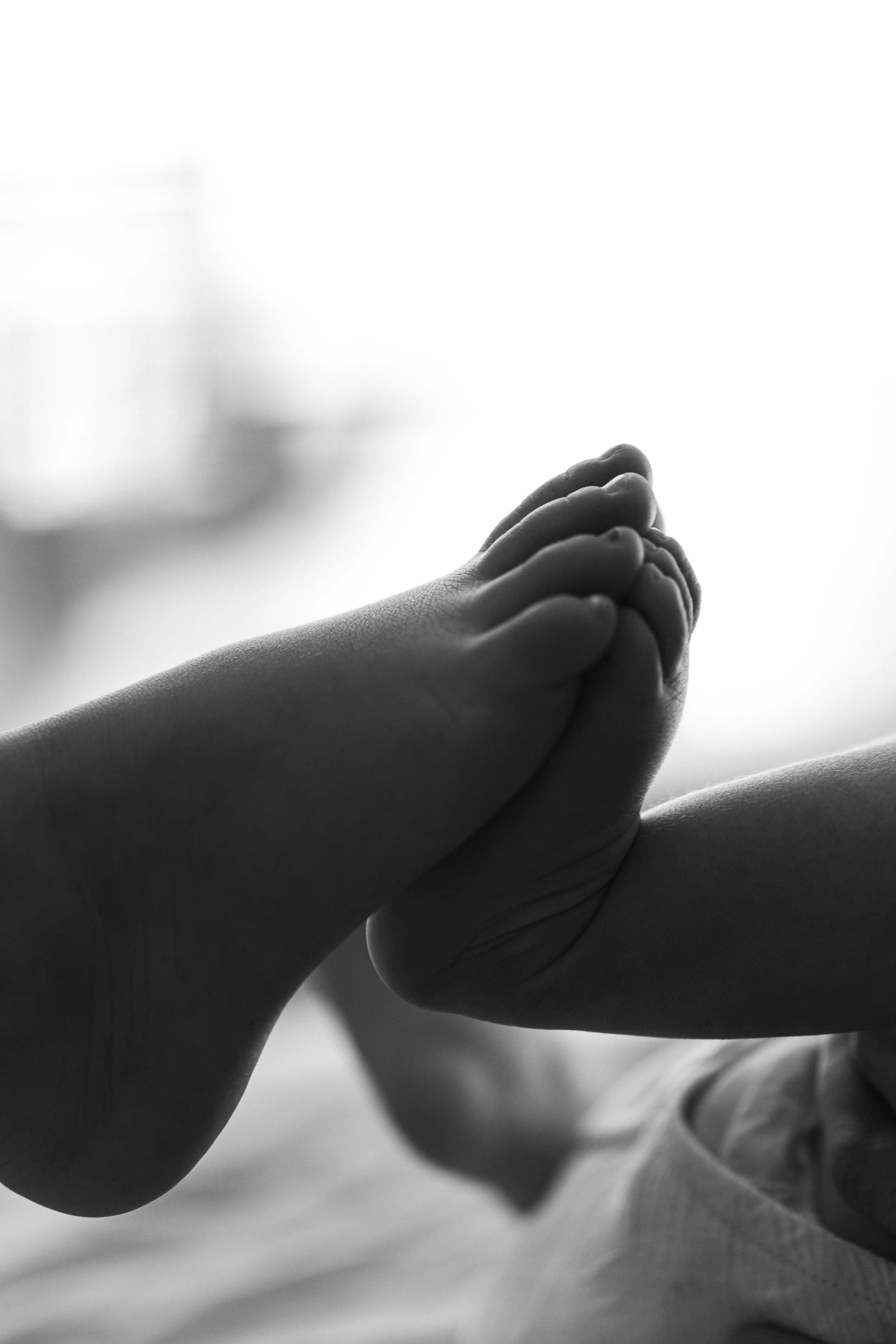 Close-up of a child's foot gently pressing against a newborn's foot, in black and white, photographed in-home by Maison Mancel in NYC.