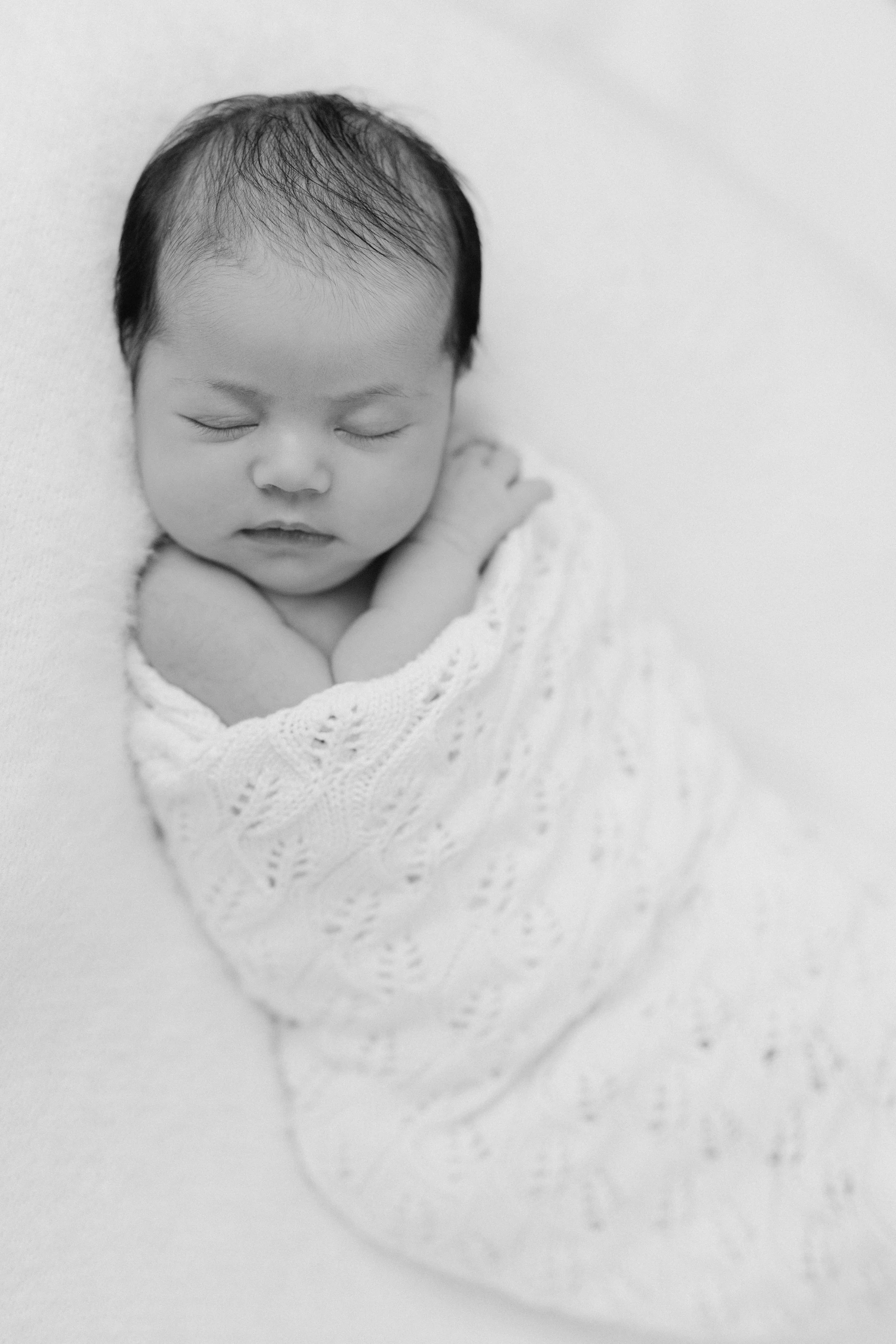 An in-home newborn portrait of a sleeping newborn baby wrapped in a knitted blanket, photographed by Maison Mancel in NYC.