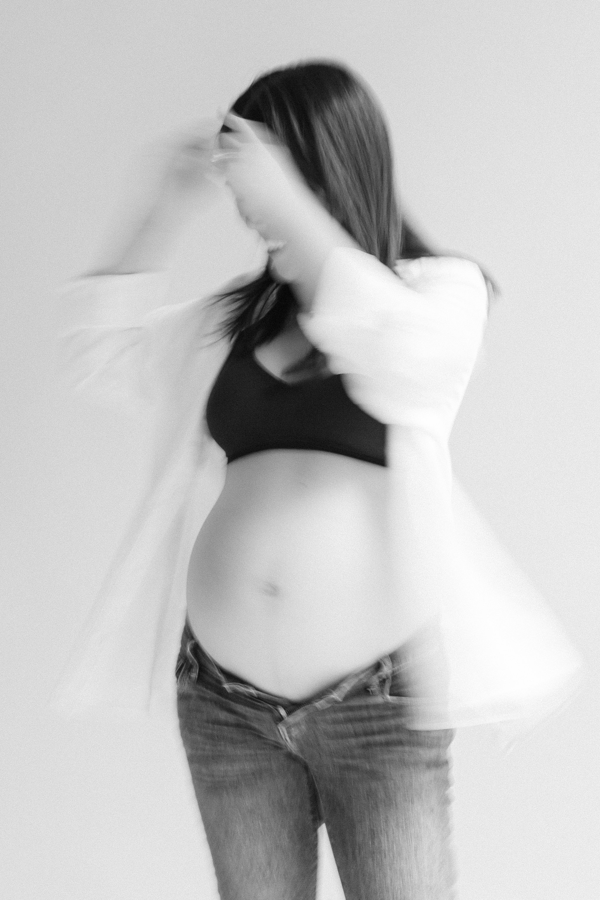 Blurry black and white photo of a woman with long hair, wearing a black top and jeans, adjusting her hair with her hand. Photographed by Maison Mancel in-studio in Brooklyn, NYC.