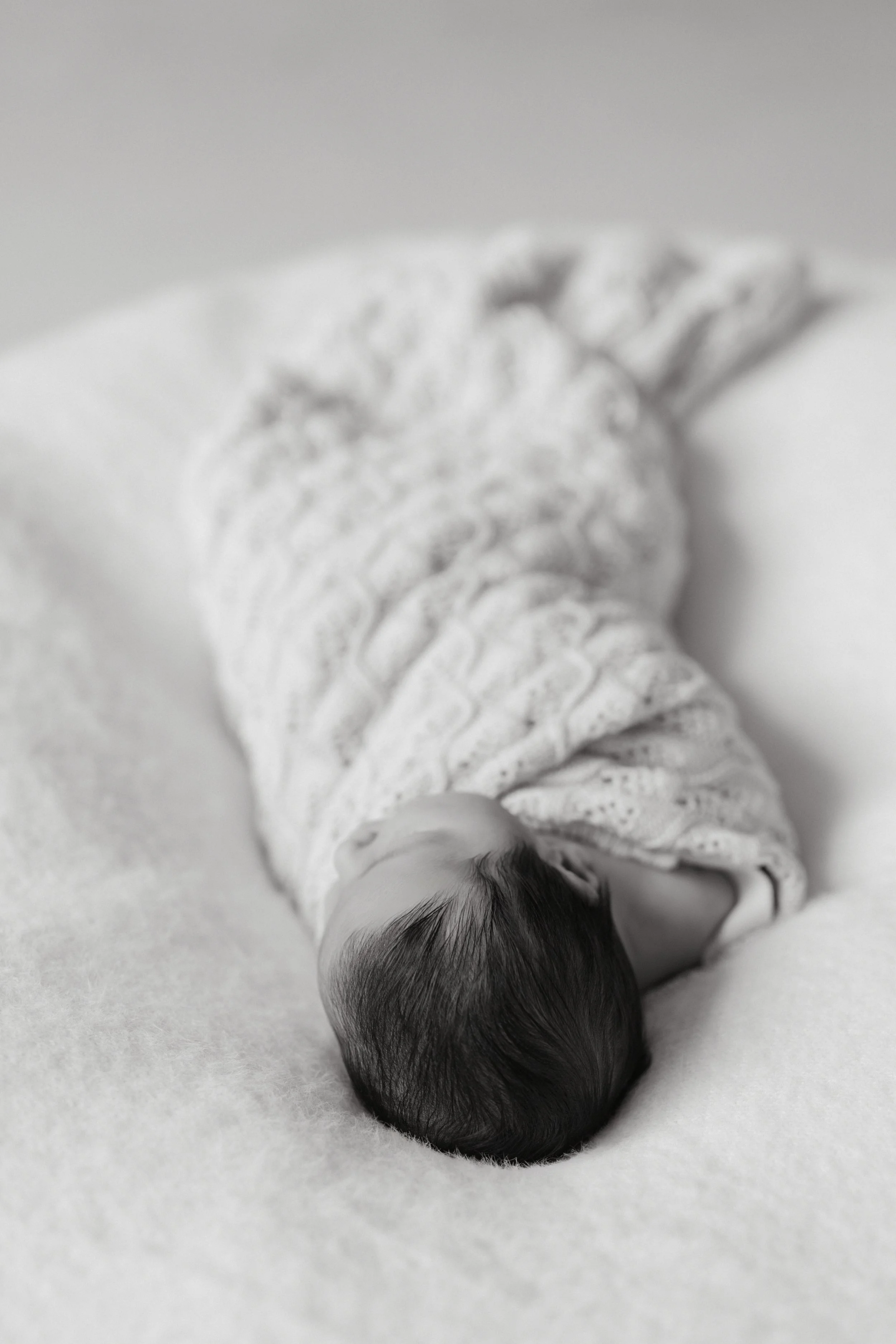 Portrait of a newborn baby sleeping on a soft surface, wrapped in a patterned blanket, photographed by Maison Mancel in NYC.
