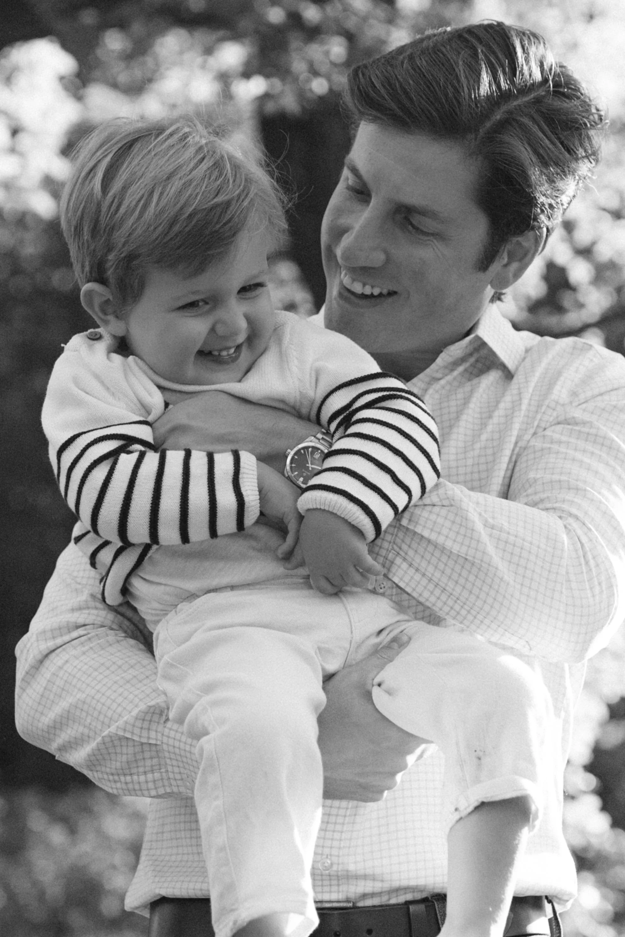 A lifestyle family portrait of a father smiling and holding a young boy in his arms outdoors, both appearing happy, photographed by Maison Mancel in Central Park.
