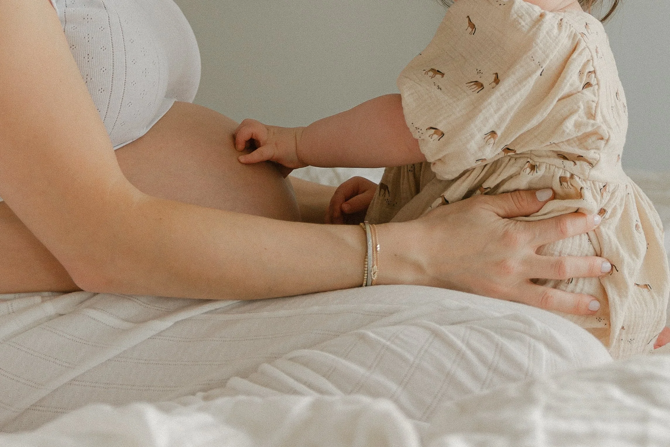 An in-home lifestyle maternity session of a pregnant woman lying on a bed holding her baby bump while a young child touches her belly. Photographed by Maison Mancel in Brooklyn.