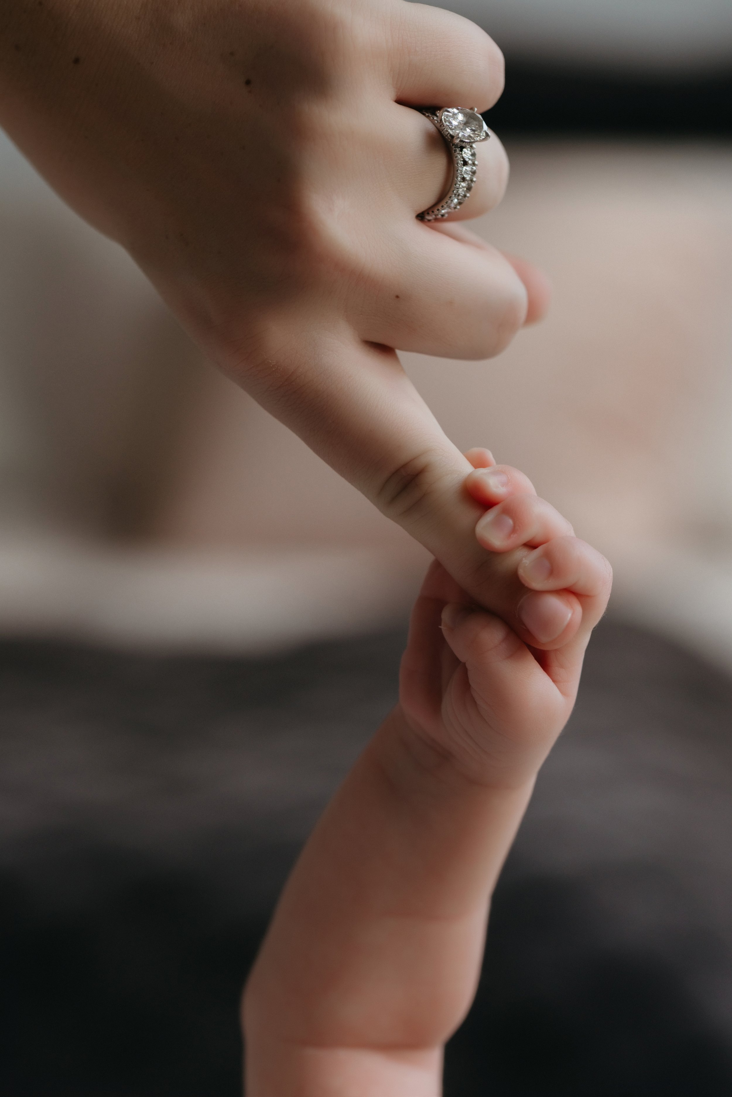 Close-up of a mother wearing a diamond engagement ring, gently touching a baby's hand with her finger, photographed in-home by Maison Mancel in Manhattan.
