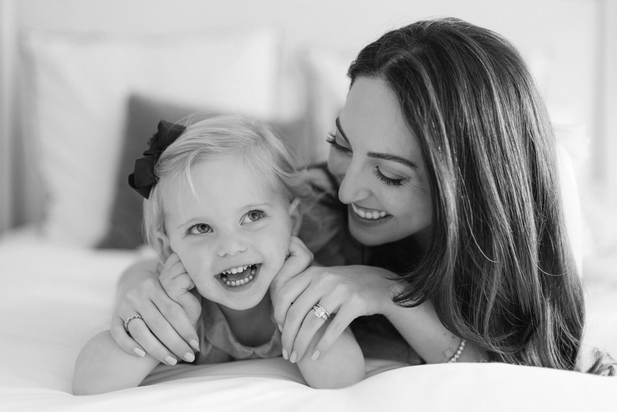A woman and a young girl are lying on a bed, smiling and interacting affectionately.