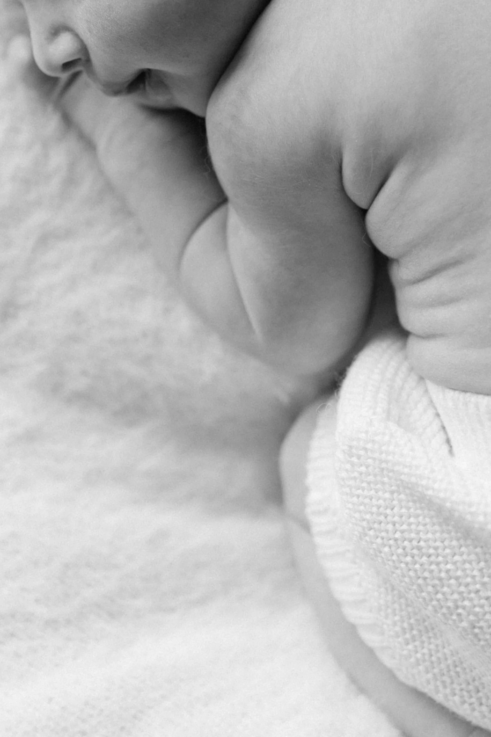 Close-up black and white photo of a sleeping newborn in-home in West Village, showing face, arm, and ear, resting on a soft fabric surface, photographed by Maison Mancel in NYC.